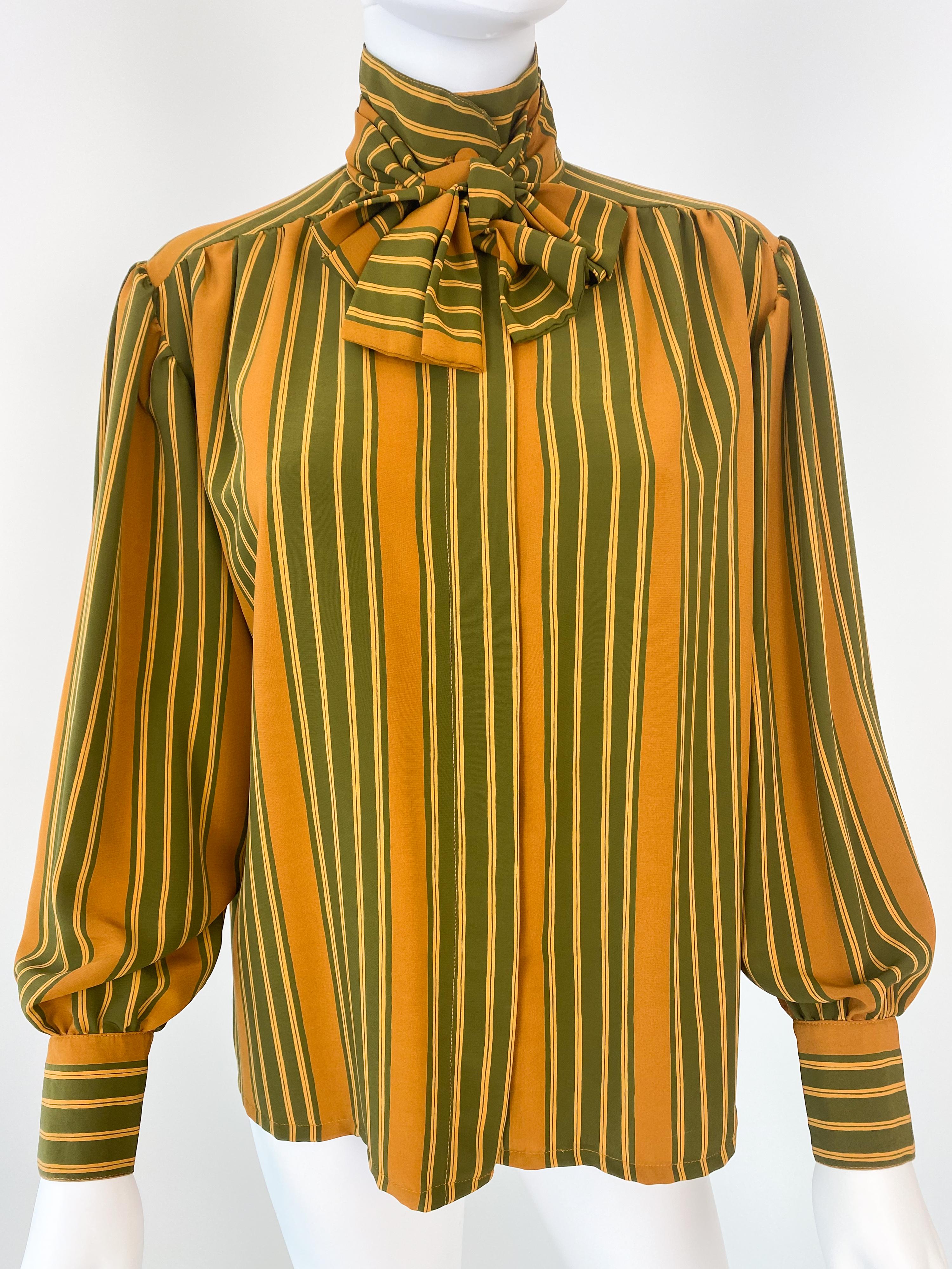 Esta impresionante blusa con lazada de los años 80 está confeccionada con una lujosa mezcla de poliéster sedoso y viscosa. Su vibrante estampado a rayas en verde aguacate y amarillo azafrán desprende encanto vintage, complementado por el original