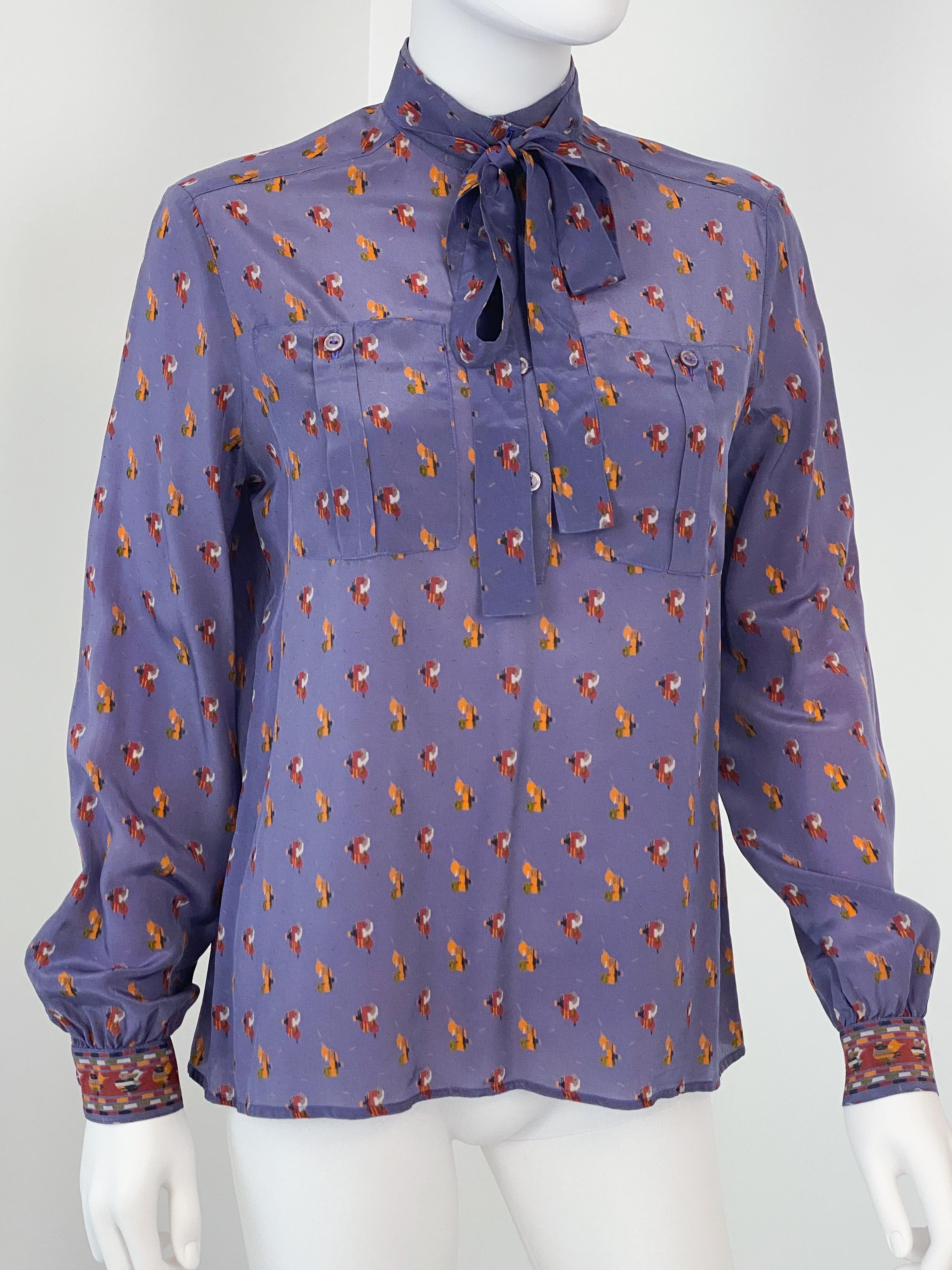 Cette exquise blouse vintage des années 1980 se compose d'un tissu soyeux en viscose de polyester d'un violet riche et éclatant, orné d'un imprimé accrocheur dans les tons orange et bordeaux. Conçu dans une charmante silhouette de style paysan, il