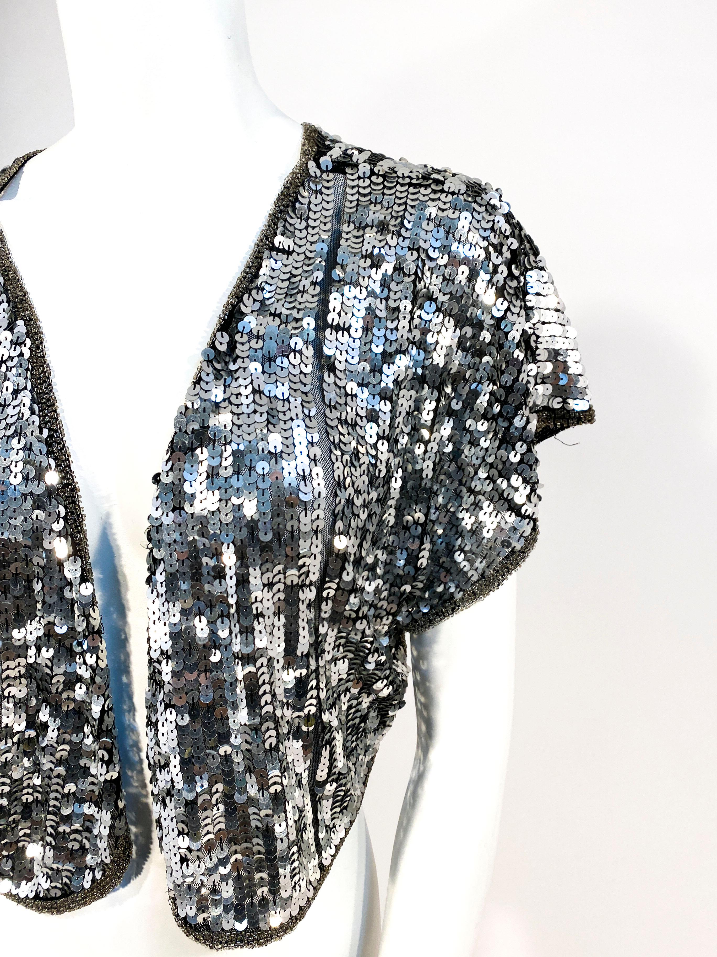 1980s silver sequin disco bolero with beaded trim and modified winged sleeves. There are symmetrical stripes on the front face with no sequin. 