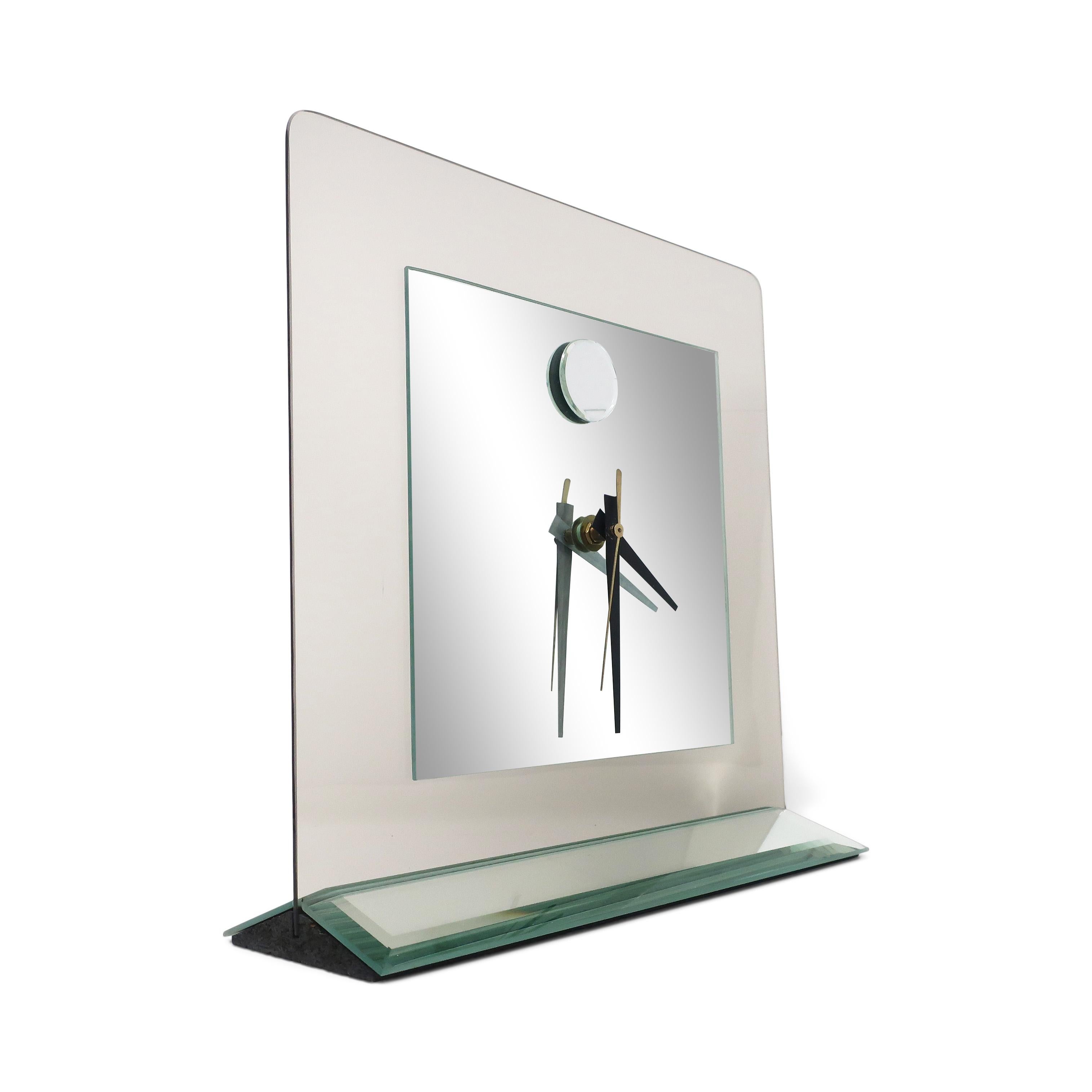 A stunning postmodern smoked glass and mirror table or mantle clock. Triangular mirrored base with beveled edges and a mirrored face with a smoked glass border featuring rounded edges. The design includes a round piece of mirror at 12 o’clock.

In