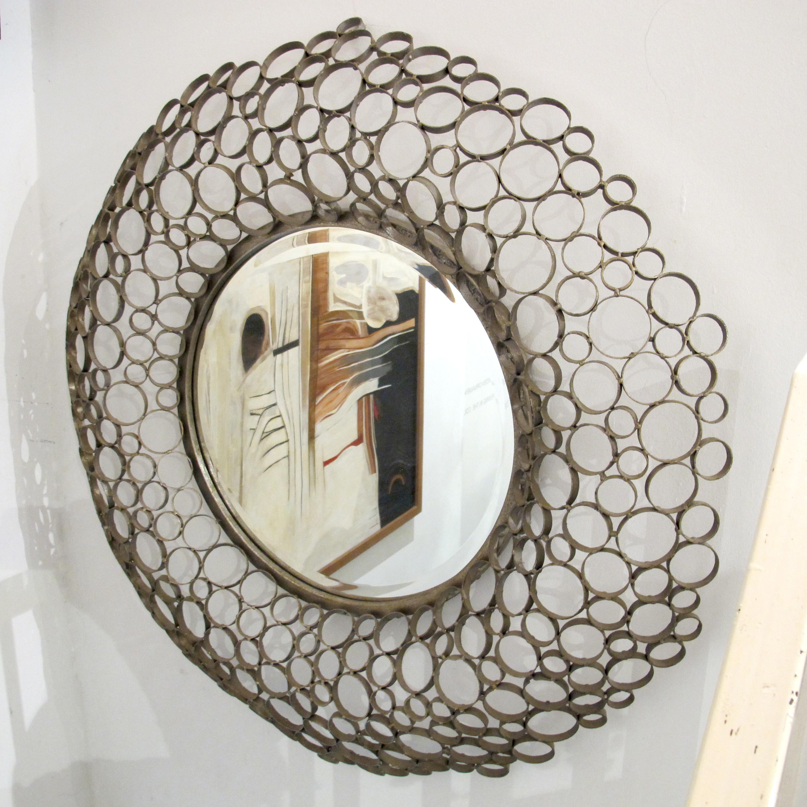 Spanish round wall mirror with a hand-made metal frame composed of interlocking circular rings in various sizes. The frame features a light bronze-toned patina and an openwork design, complemented by a central bevelled mirror, dating from the 1980s;