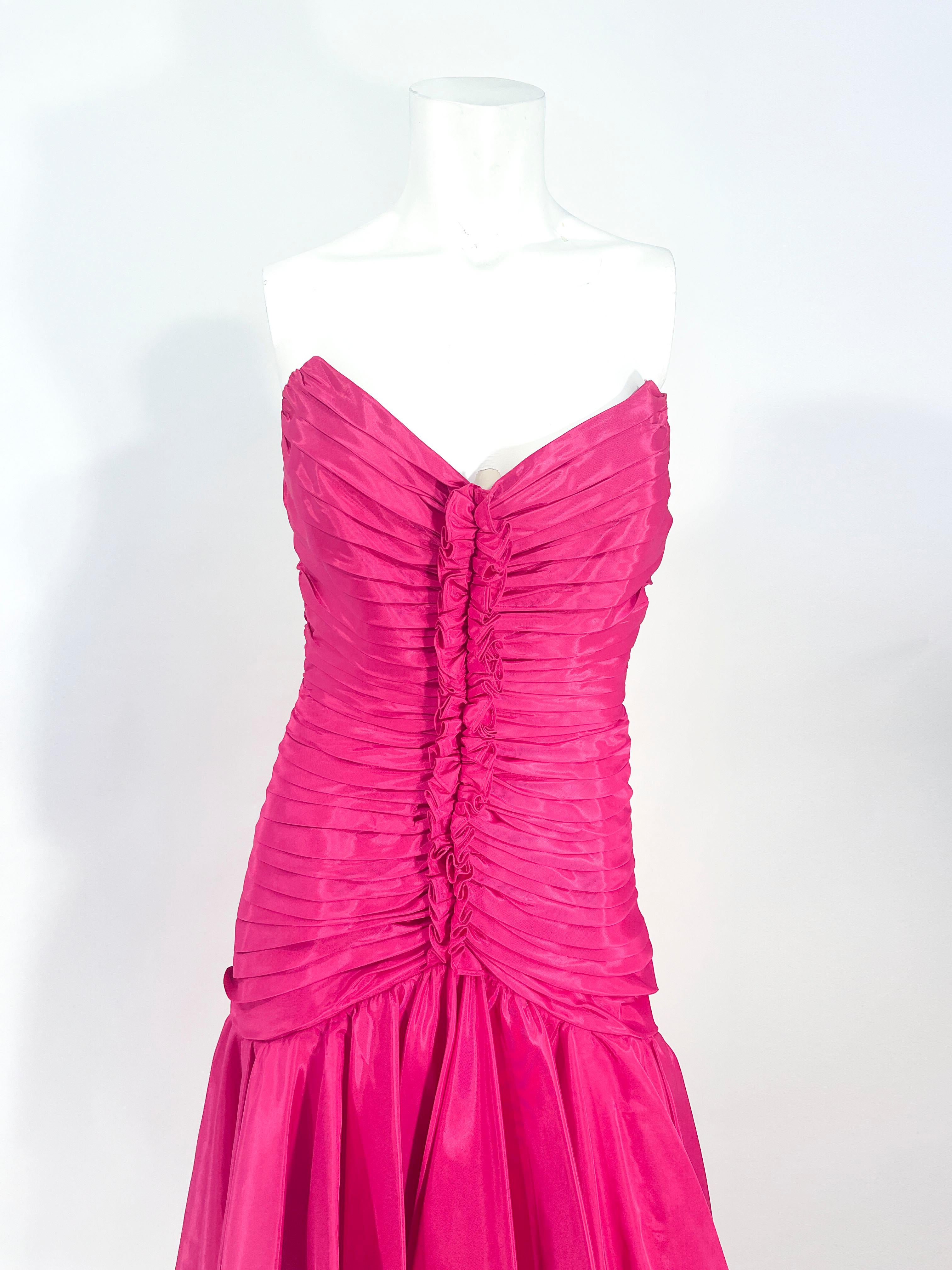 1980s Tadashi hot pink cocktail dress featuring a strapless/sleeveless neckline, pleated and ruching coming to a central vertical ruffle. The ruching and pleating go down past the hipline and open up to the high-low layered taffeta over chiffon