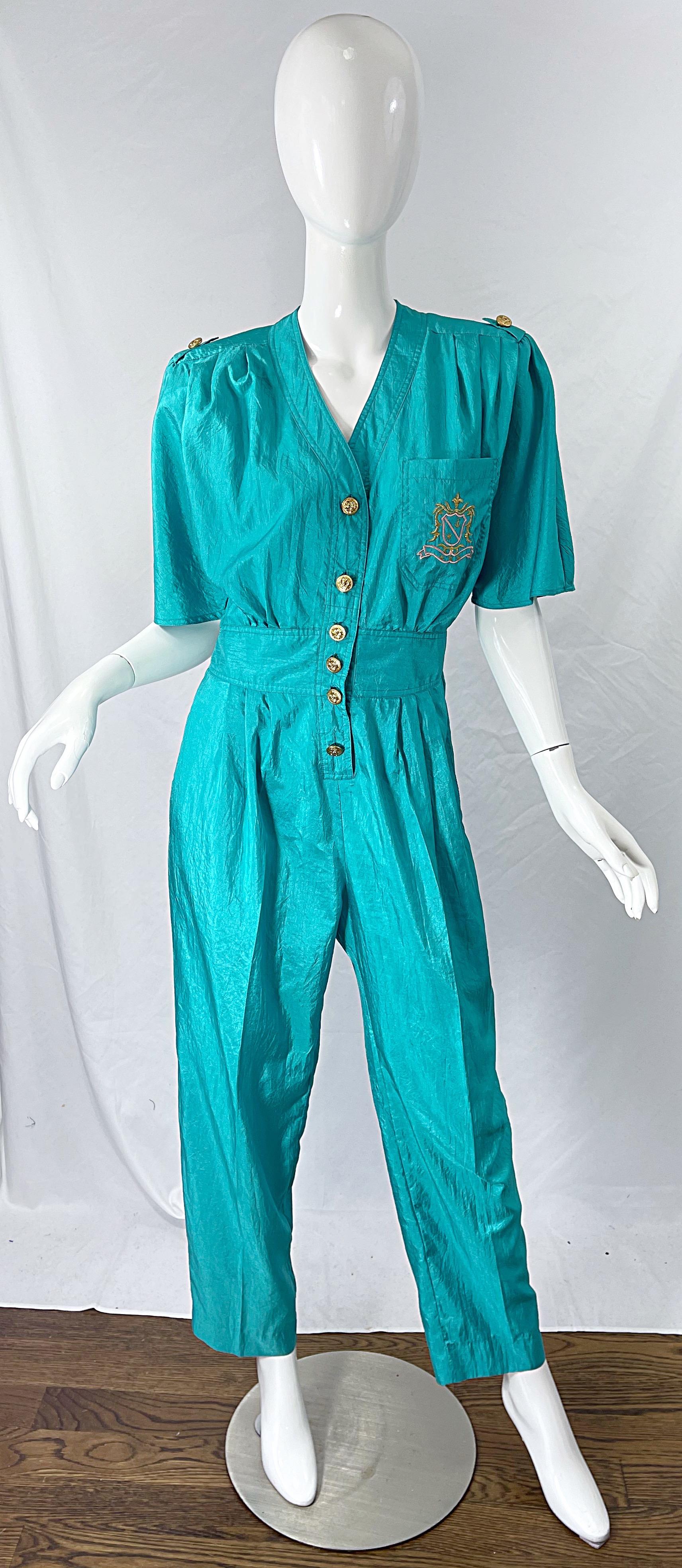 Chic 1980s teal blue green jumpsuit ! The perfect teal color that looks fantastic on any skin tone. Crescent embroidered detail in pink and gold at left breast pocket. Soft lightweight windbreaker fabric. 
Anchor embossed gold buttons up the front.