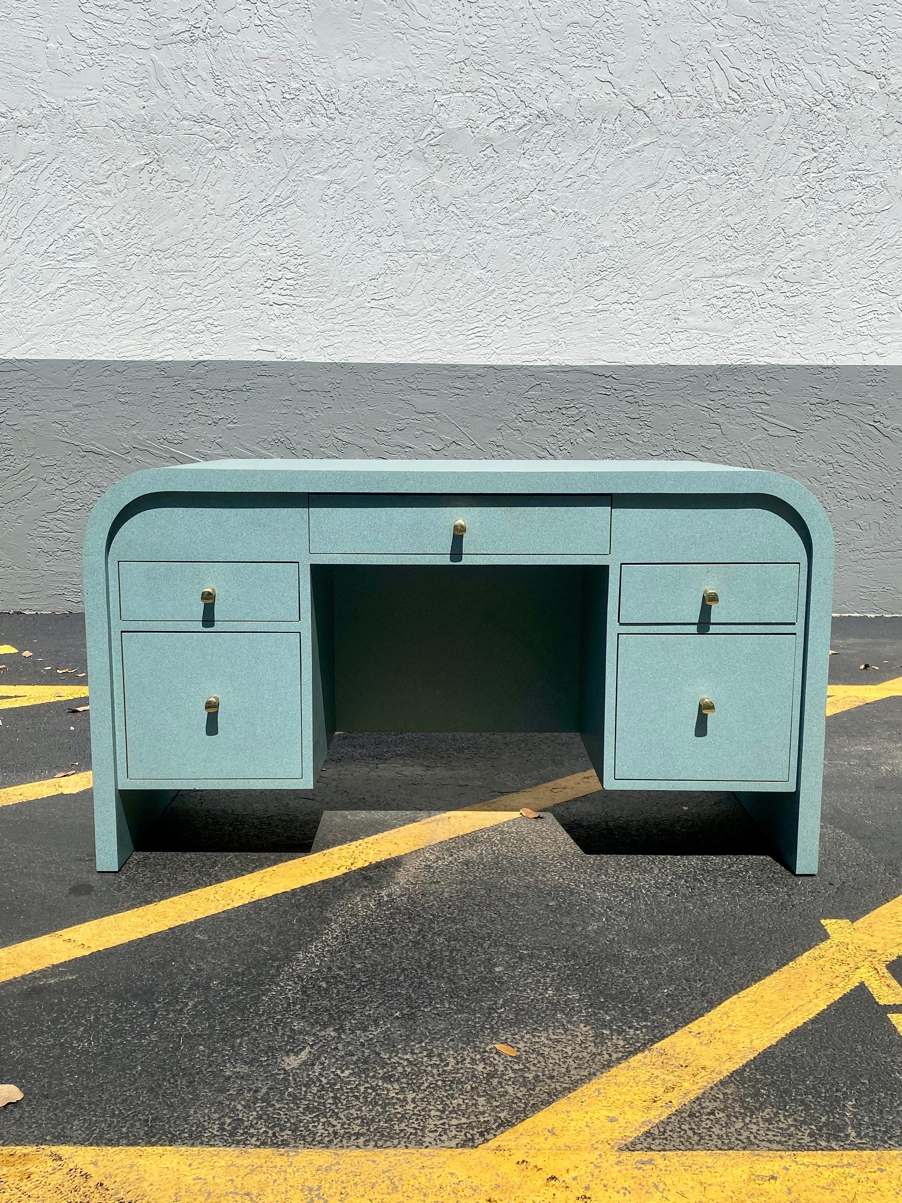 On offer on this occasion is one of the most stunning and one of a kind, Tiffany teal laminate over solid wood desk you could hope to find. Outstanding design is exhibited throughout. Cane back details with brass hardware. The beautiful desk is