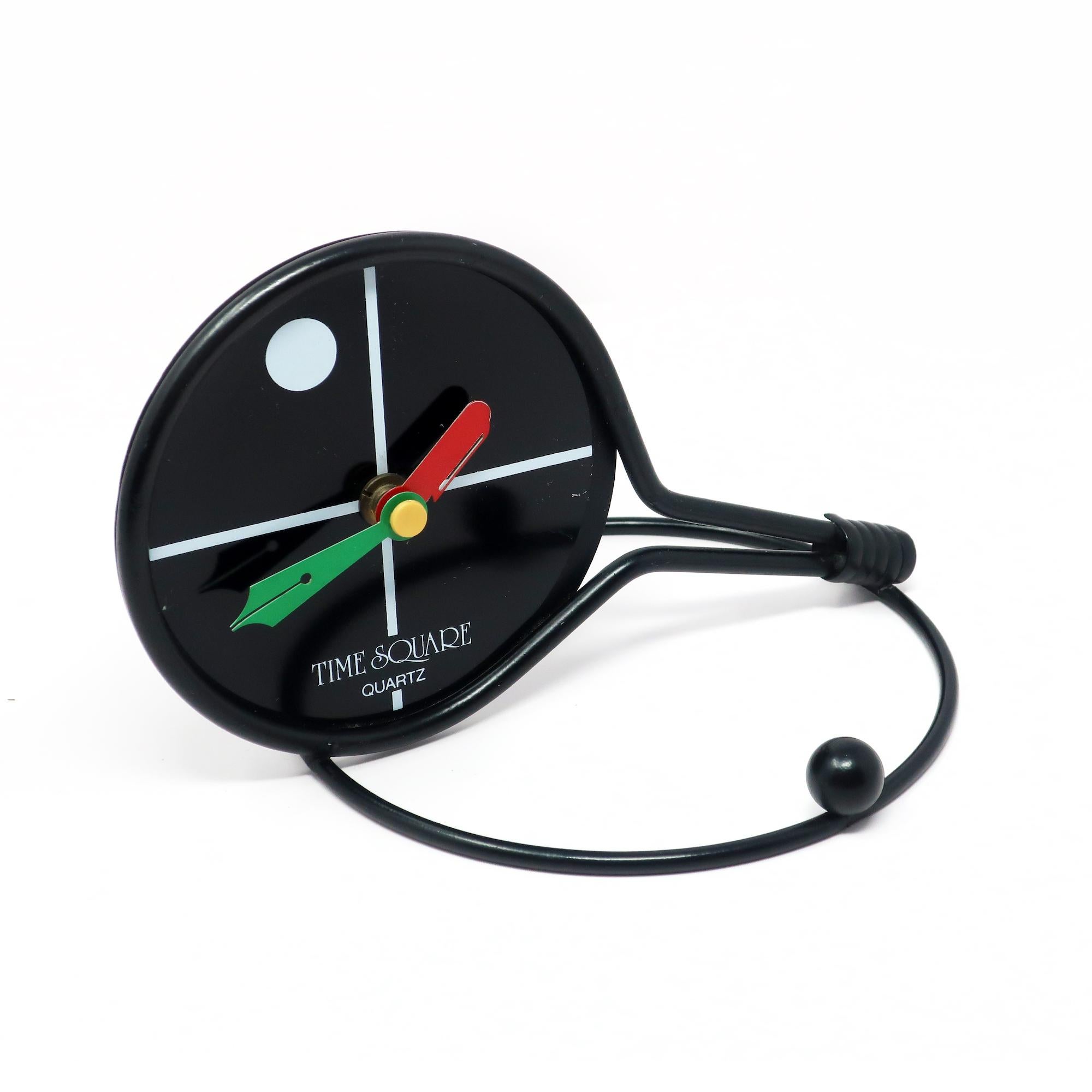 A whimsical desk or shelf clock in the shape of a tennis racket hitting a ball. Black metal racket, ball, and stand with a black face with red, green, yellow, and white accents. Perfect for tennis lovers or fans of whimsical clocks and other