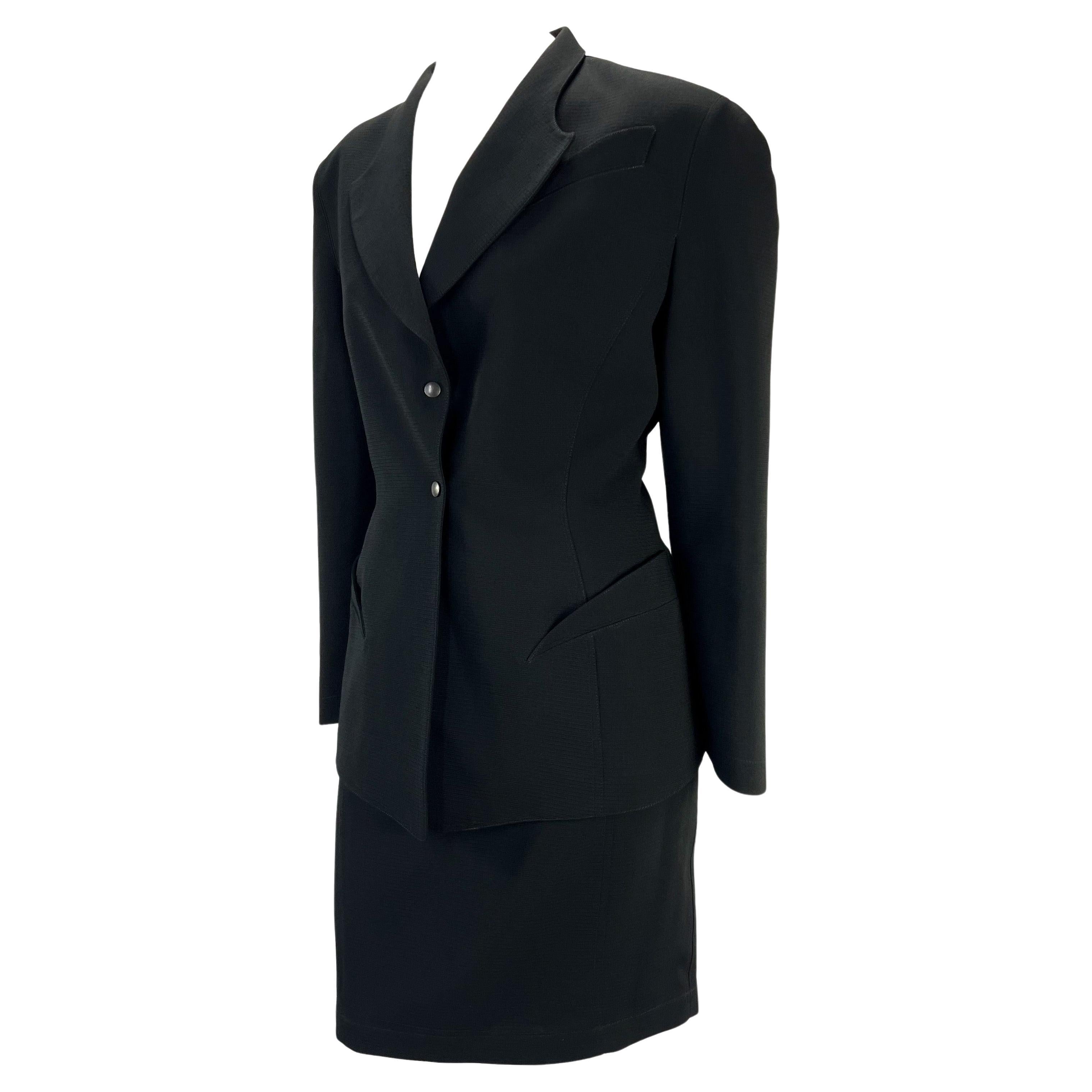 Presenting a sculptural black Thierry Mugler skirt suit, designed by Manfred Mugler. From the 1980s, this suit features masterful design and tailoring. The blazer features sculptural curved faux pockets which extenuate the hips. Both the skirt and