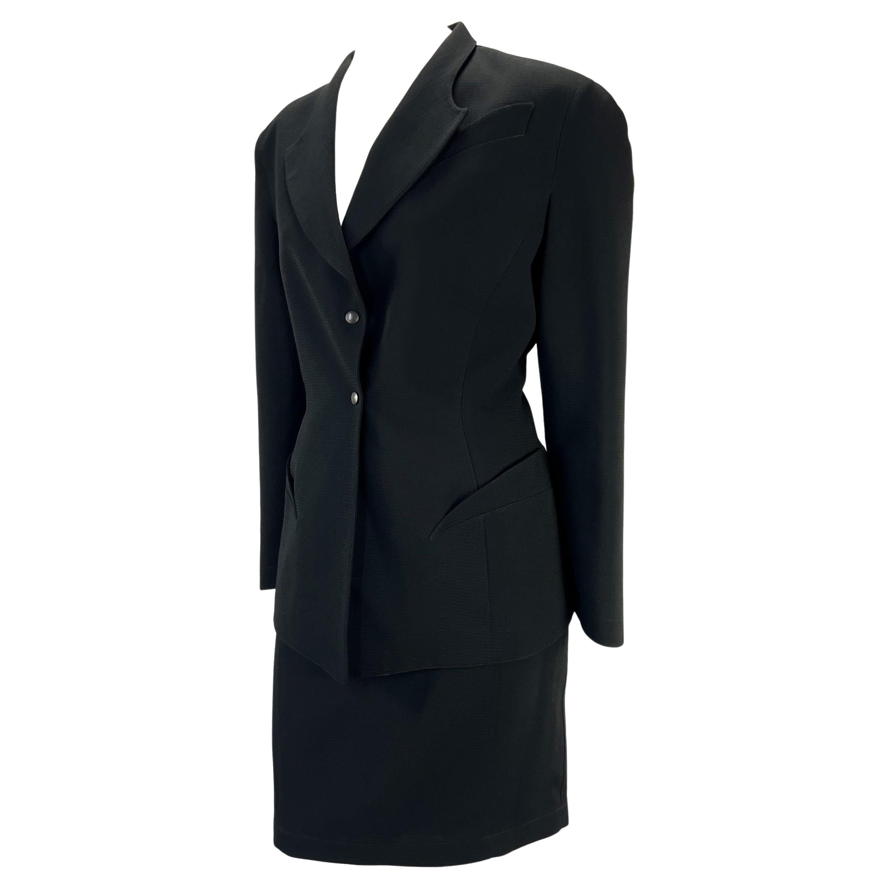 Presenting a sculptural black Thierry Mugler skirt suit designed by Manfred Mugler. From the 1980s, this suit features masterful design and tailoring. The blazer features sculptural curved faux pockets which extenuate the hips. The skirt and blazer