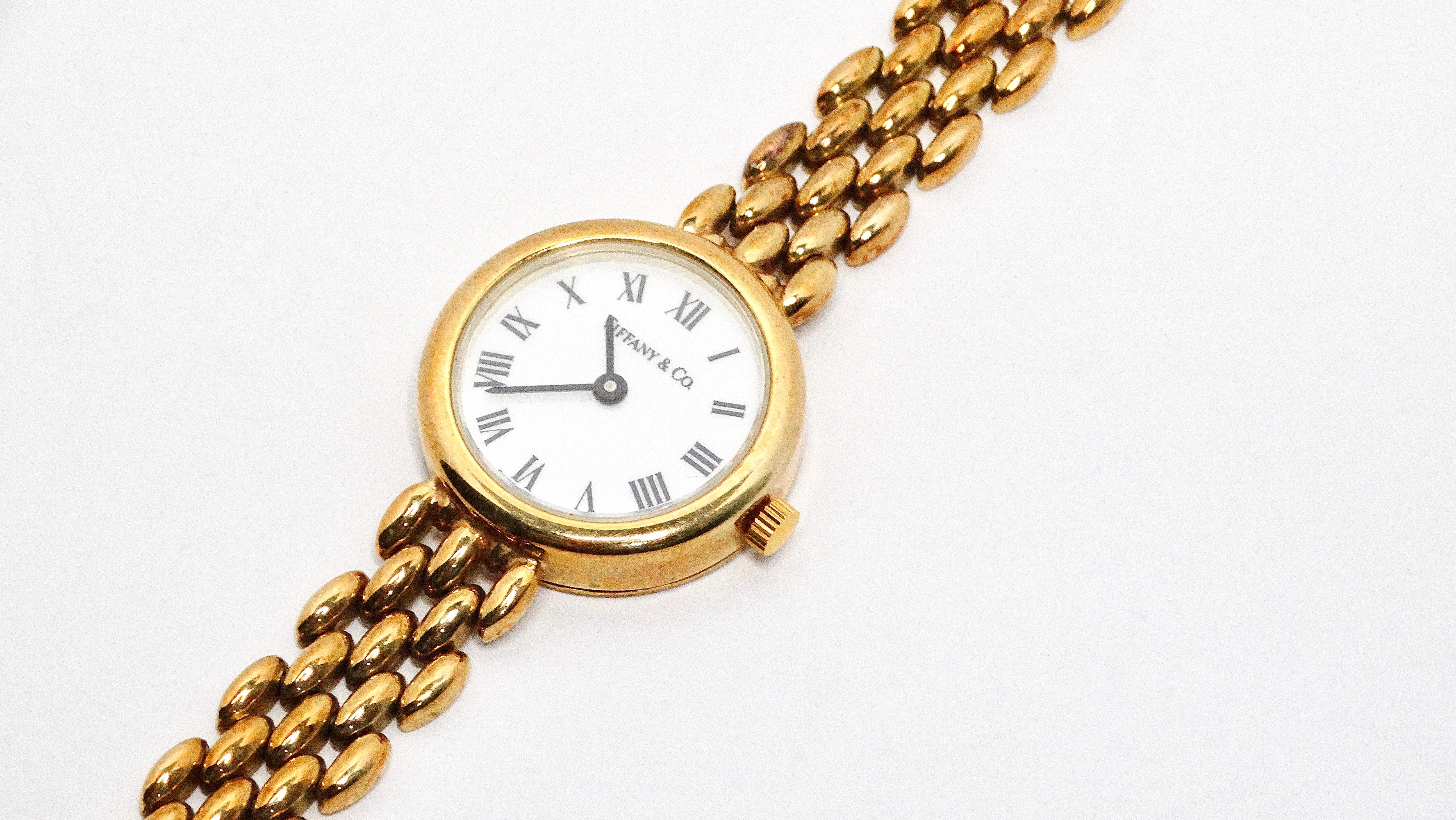 The 1980s Tiffany & Co. 14k Yellow Gold Round Face Classic Wristwatch is a vintage masterpiece, featuring a white dial with striking black Roman numerals that exude timeless elegance. The watch's sleek design is highlighted by a thin 14k gold band