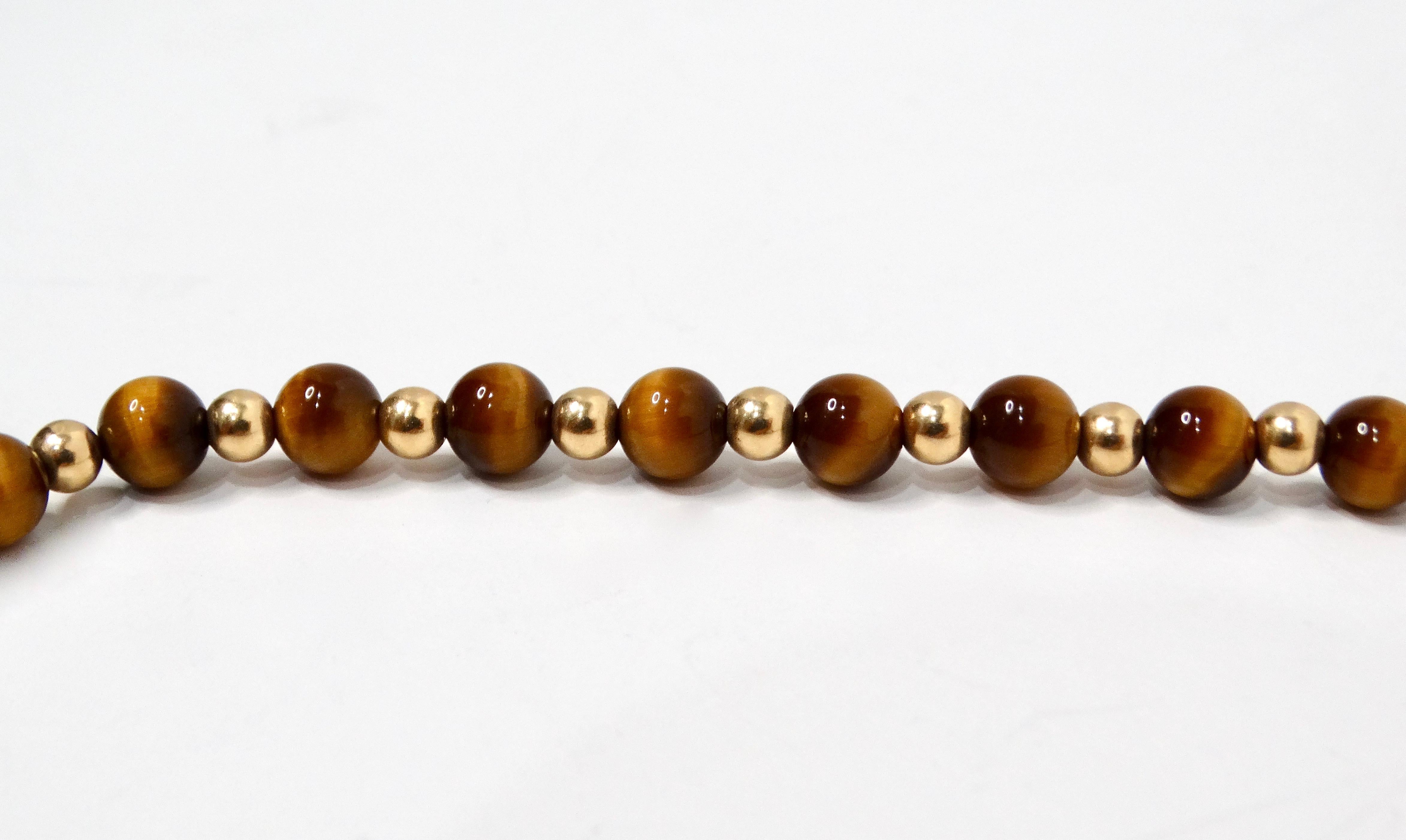 Ce superbe collier long en or jaune 14k et œil de tigre des années 1980 est une pièce remarquable qui marie merveilleusement l'élégance vintage à la sophistication moderne. Fabriqué à partir de perles d'œil de tigre riches et chaudes, réputées pour