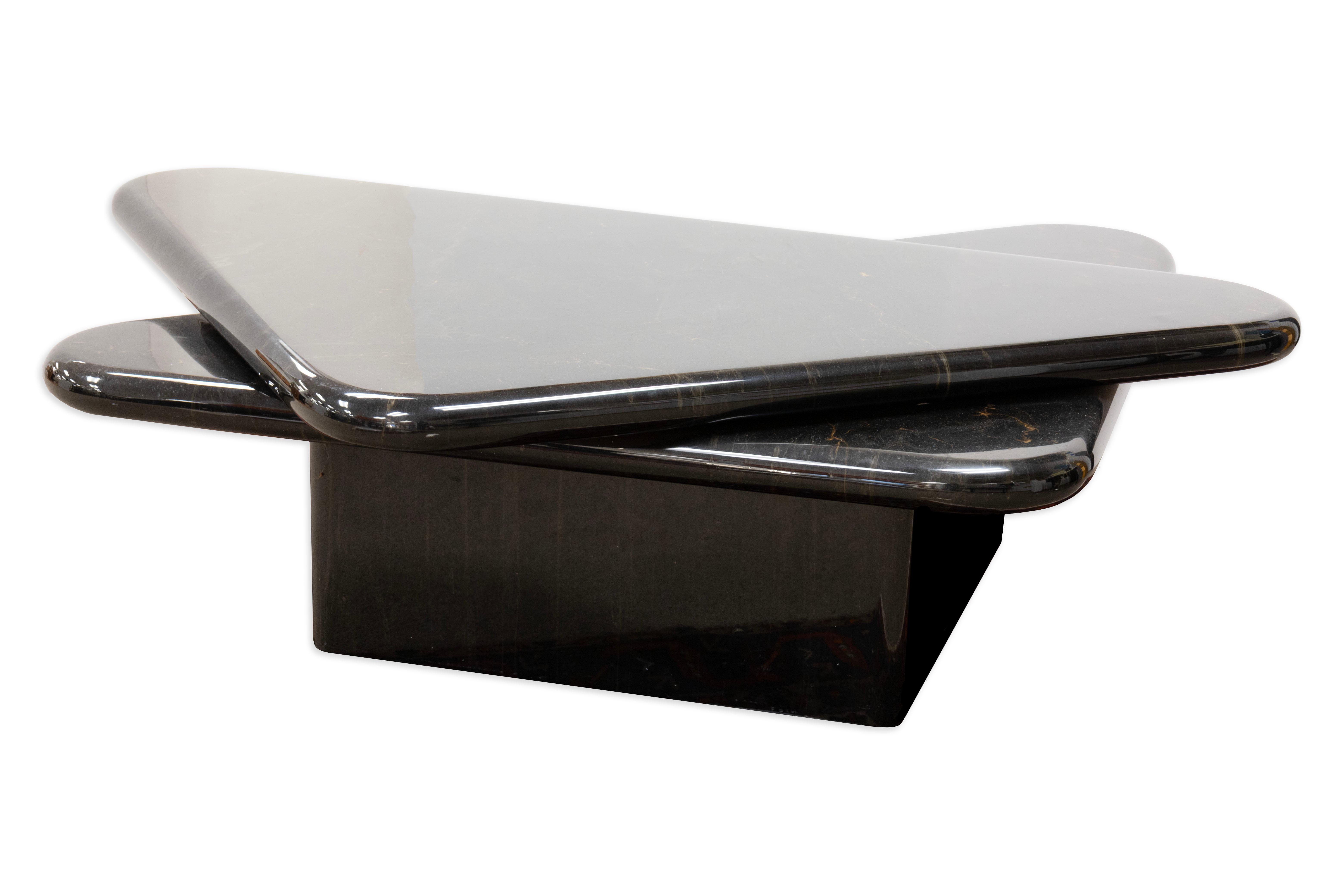 This 1980s coffee table features a bold geometric design centered around two stacked triangular tops that swivel smoothly to expand into a square or fold back into a compact, layered form. Finished in a glossy black faux marble, the surfaces display
