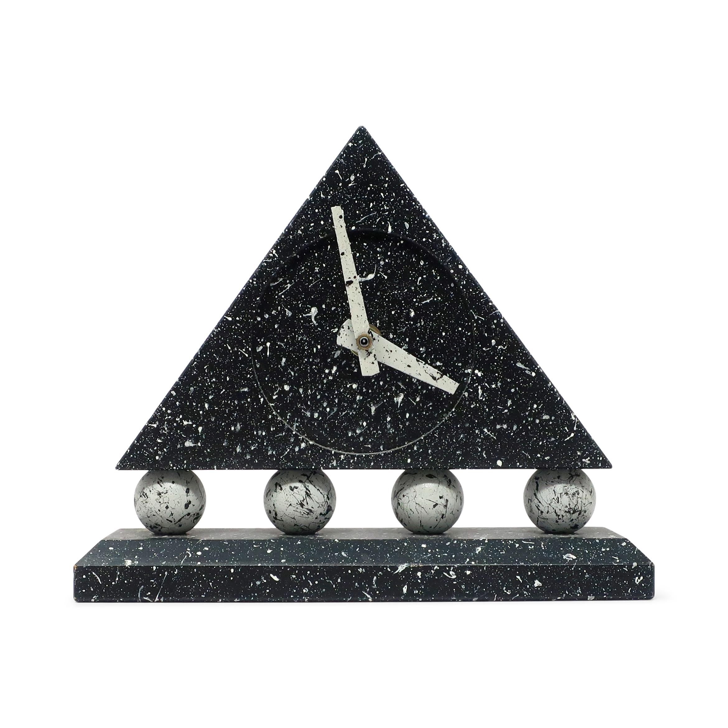 A stunning postmodern desk clock with dark gray rectangular base, round light gray supports, and dark gray triangular body with white hands.  The bold colors were then splattered with contrasting paint colors to make the whole clock pop.  

In good