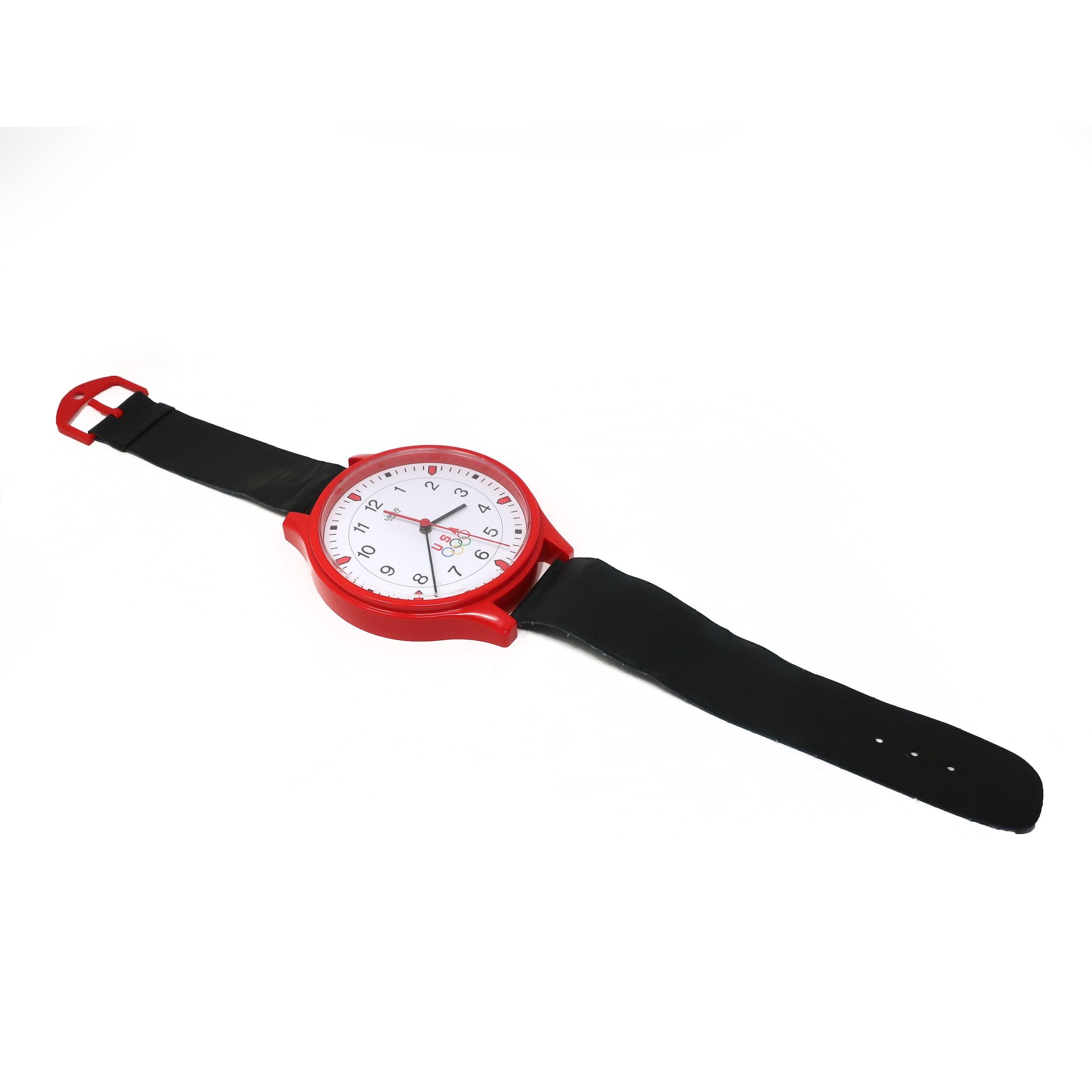 A 1980s USA Olympics clock in the shape of a wristwatch manufactured by Lorus. Likely released to commemorate the 1984 Los Angeles Olympics, this wall clock has a white face, black and red hands, black numbers, a red case, black straps, and a red