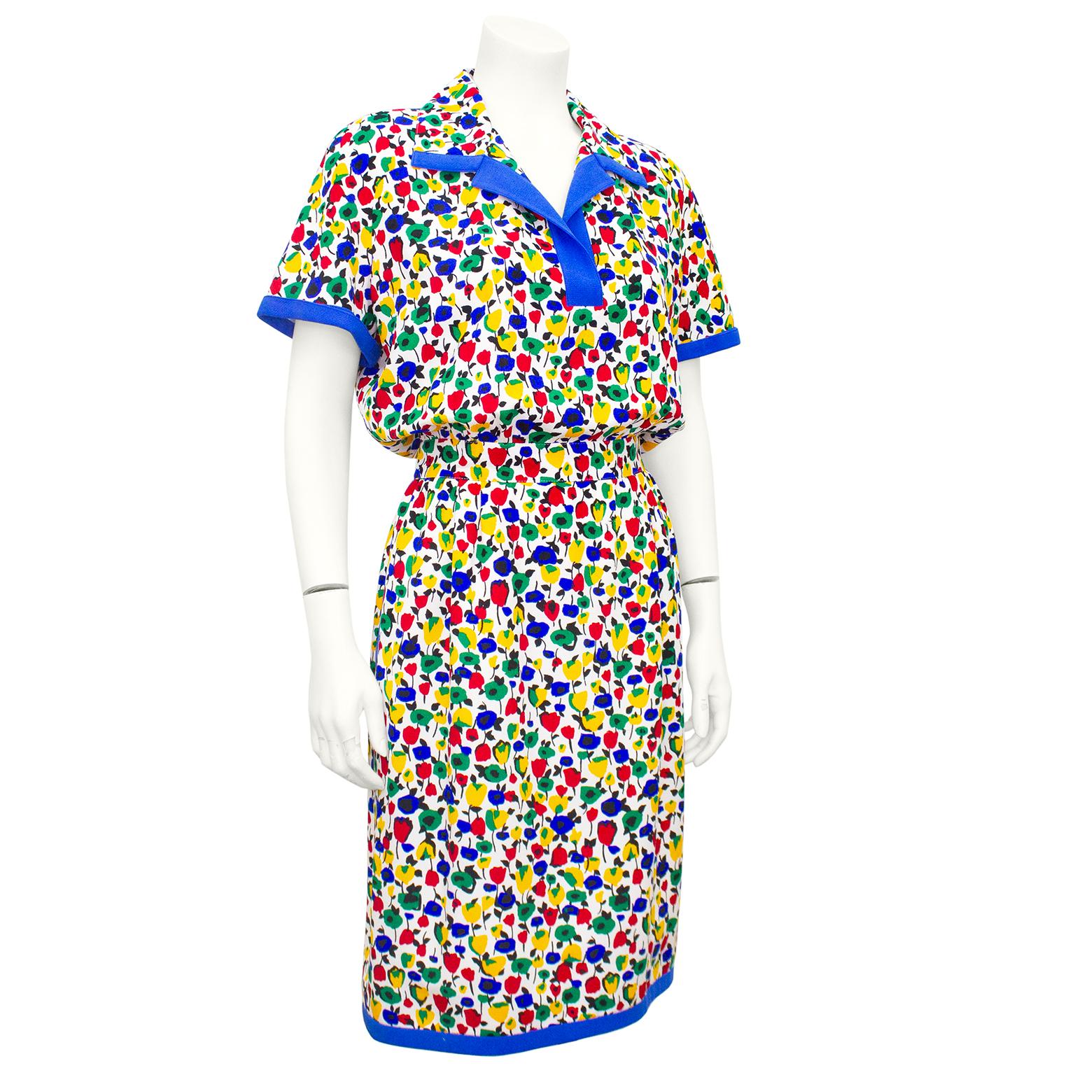 1980s Valentino summer shirt dress. White with all over red, blue, green and yellow flowers with black stems and leaves. Thick blue trim. Notched collar with open v neck, short rolled sleeves and pockets. Top is loose through the body and skirt is