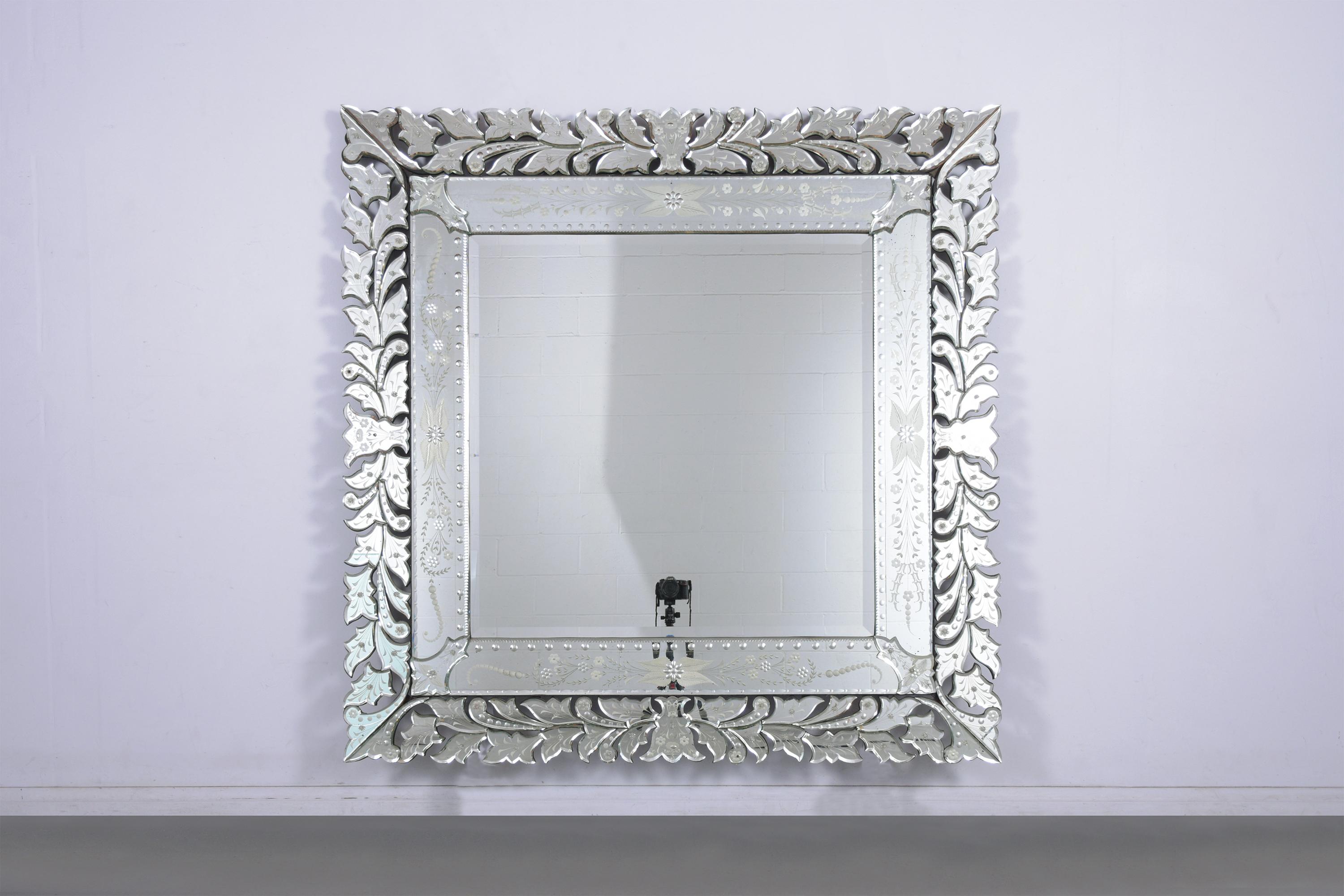 Un miroir mural de style vénitien extraordinairement travaillé, cette pièce accrocheuse est dotée d'un miroir central biseauté qui est entièrement réfléchissant et encadré par une bordure de pièces de verre au design unique de fleurs et de feuilles