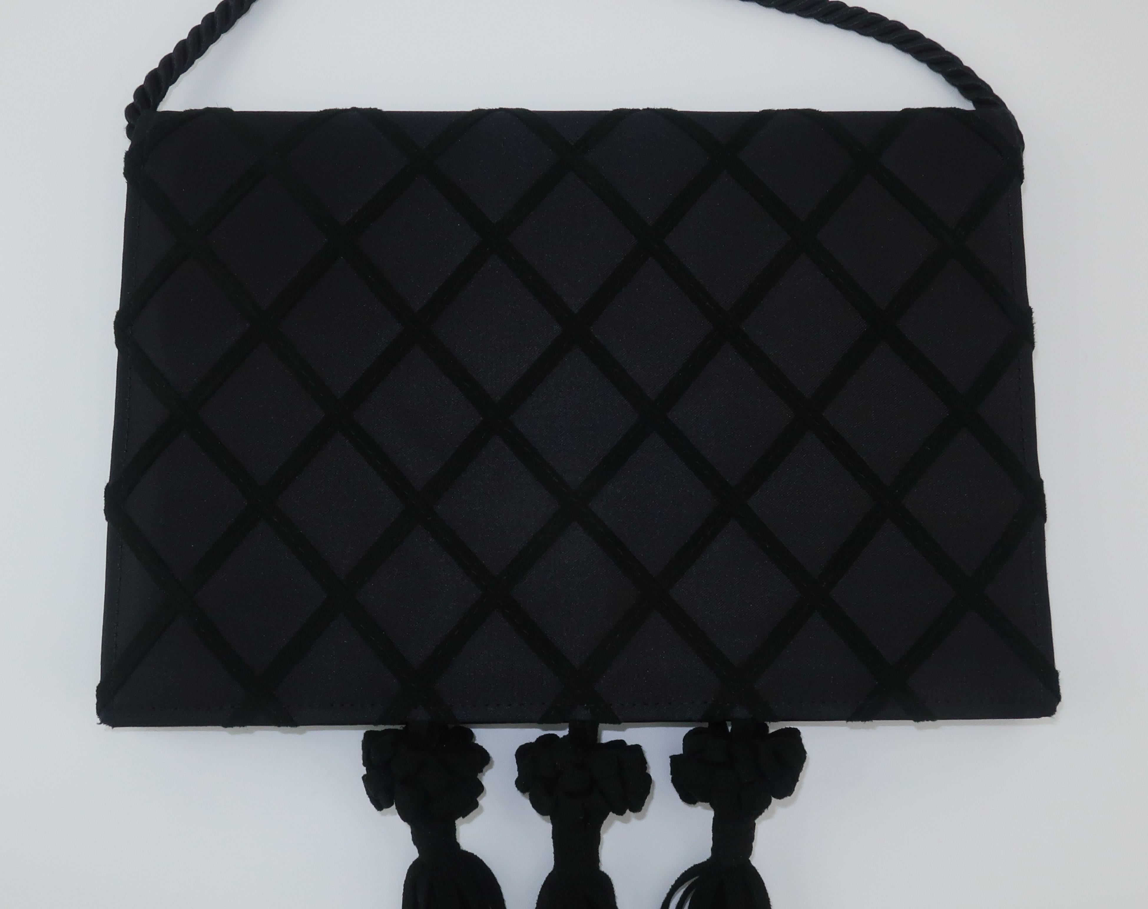 A black satin envelope style evening handbag from Victor Costa with an ultra suede lattice pattern and dangling tassels.  it features a black silk ‘rope’ drop-in shoulder strap and a snap front closure which opens to a roomy interior.  Truly a