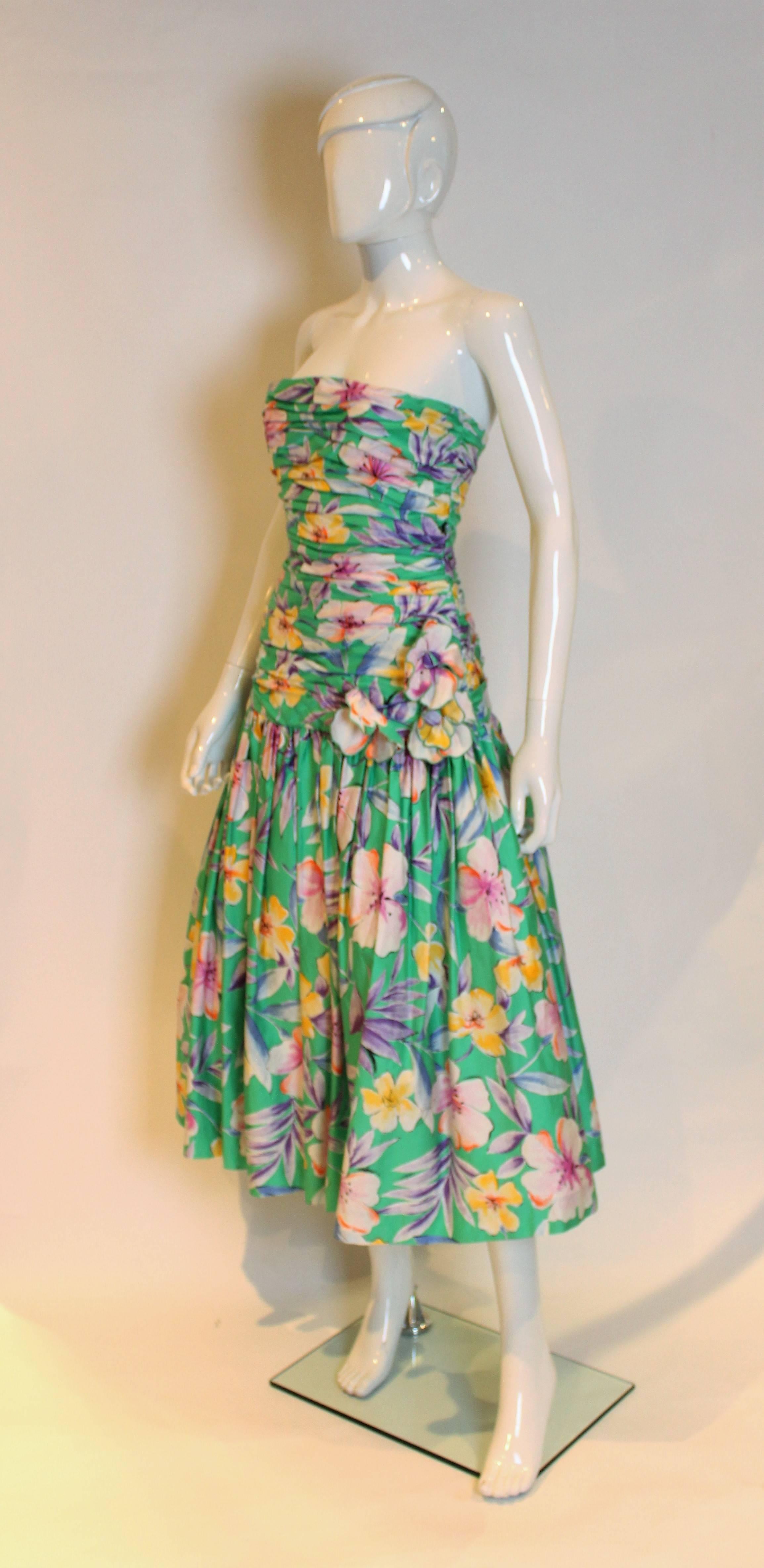 A lovely party dress by American designer Victor Costa. This dress is in a wonderful floral print on a green background. dress has gathering down to hip leval, with three self fabric flowers attached at hip level. The lower skirt has two layers of
