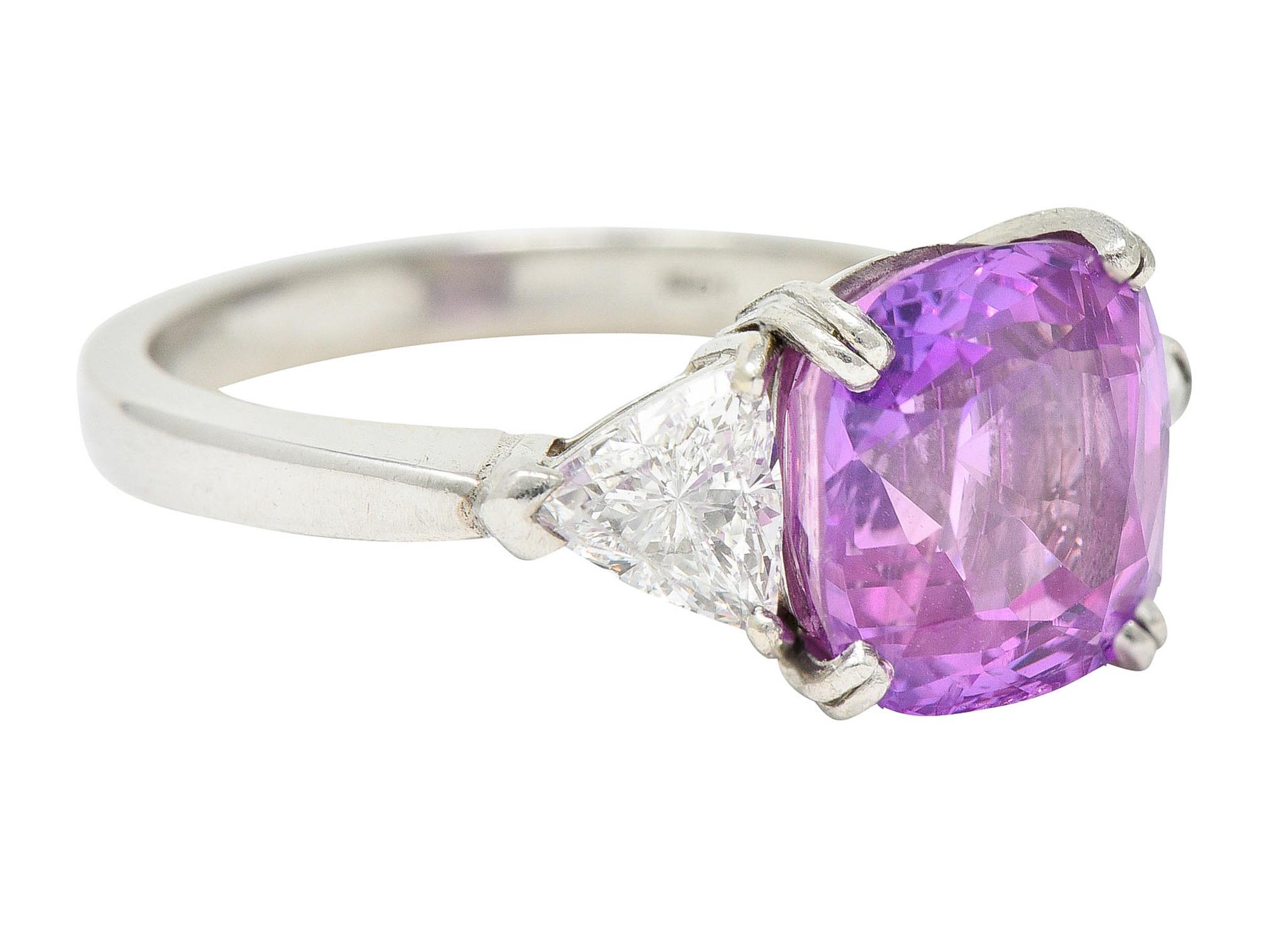 Three stone ring centers a cushion cut pink sapphire

Violetish pink in color while weighing approximately 5.40 carats

Basket set with split prongs and flanked by trilliant cut diamonds

Weighing in total approximately 0.80 carat with H/I color and
