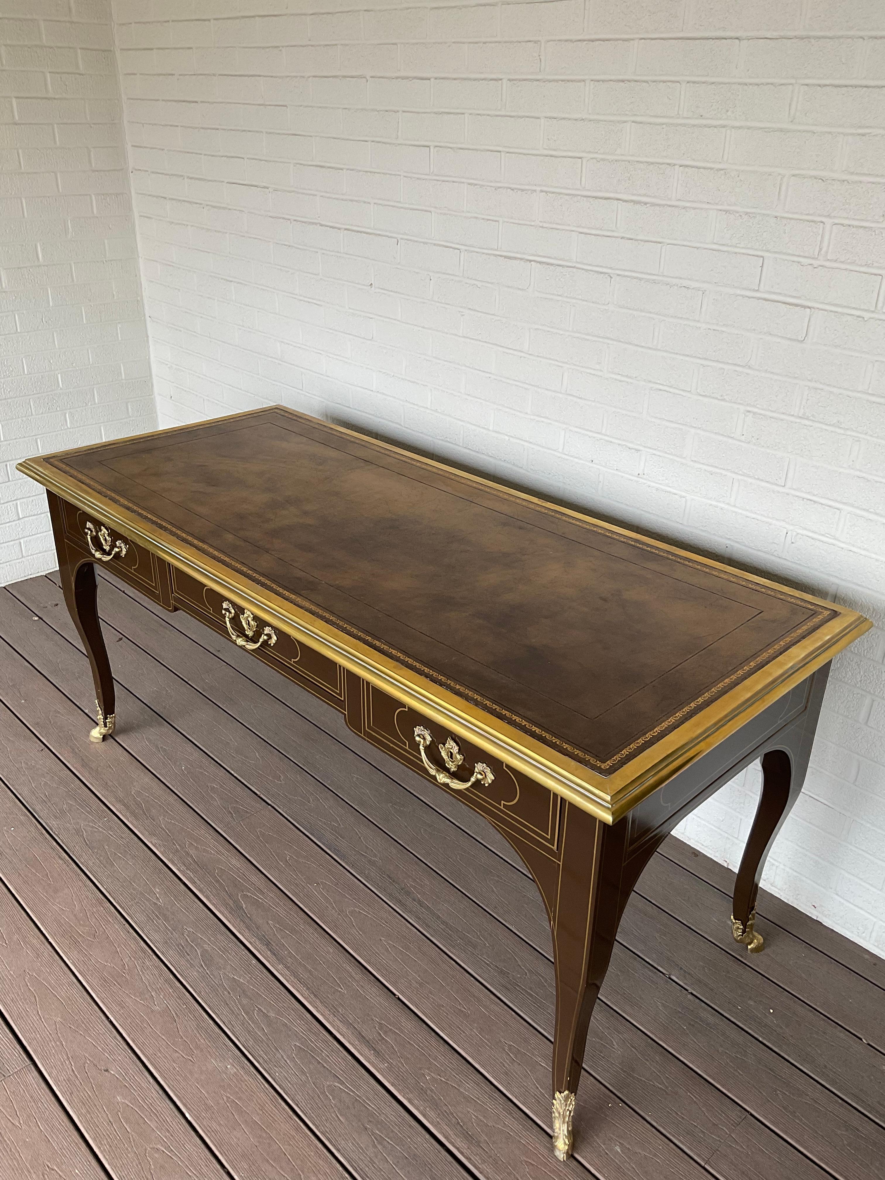 Brilliantly collaborative effort from Baker Furniture and Baker owned Mastercraft. Extraordinary chocolate brown lacquered finish with hand painted striping detailing. Large heavy brass boarder surrounds a hand tooled leather top. Gorgeous brass