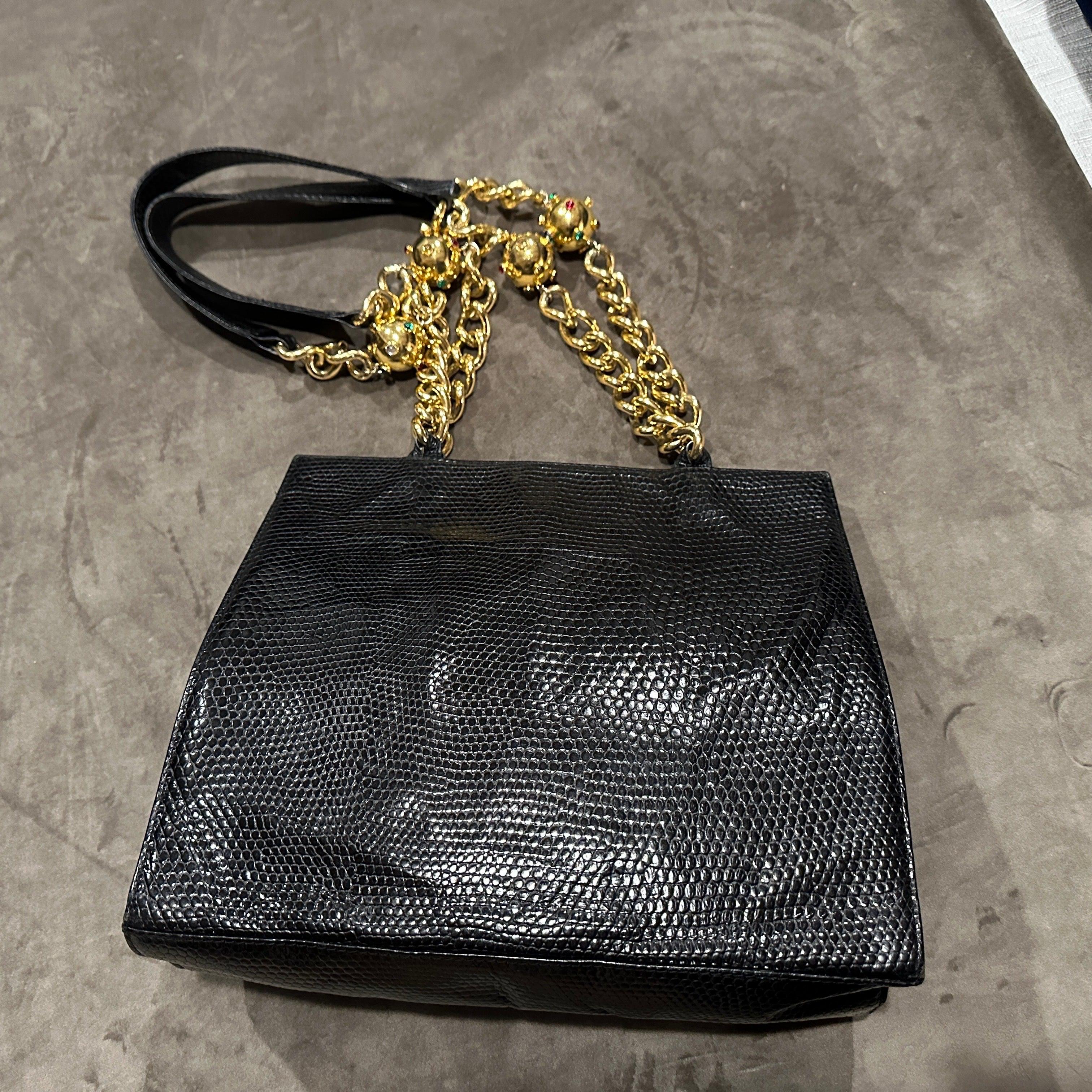 This striking vintage Italian shoulder bag is a dramatic blend of luxury and bold design, a real statement piece. Crafted in rich, black leather with a lizard or snakeskin texture, the structured silhouette of the bag lends it a sophisticated and