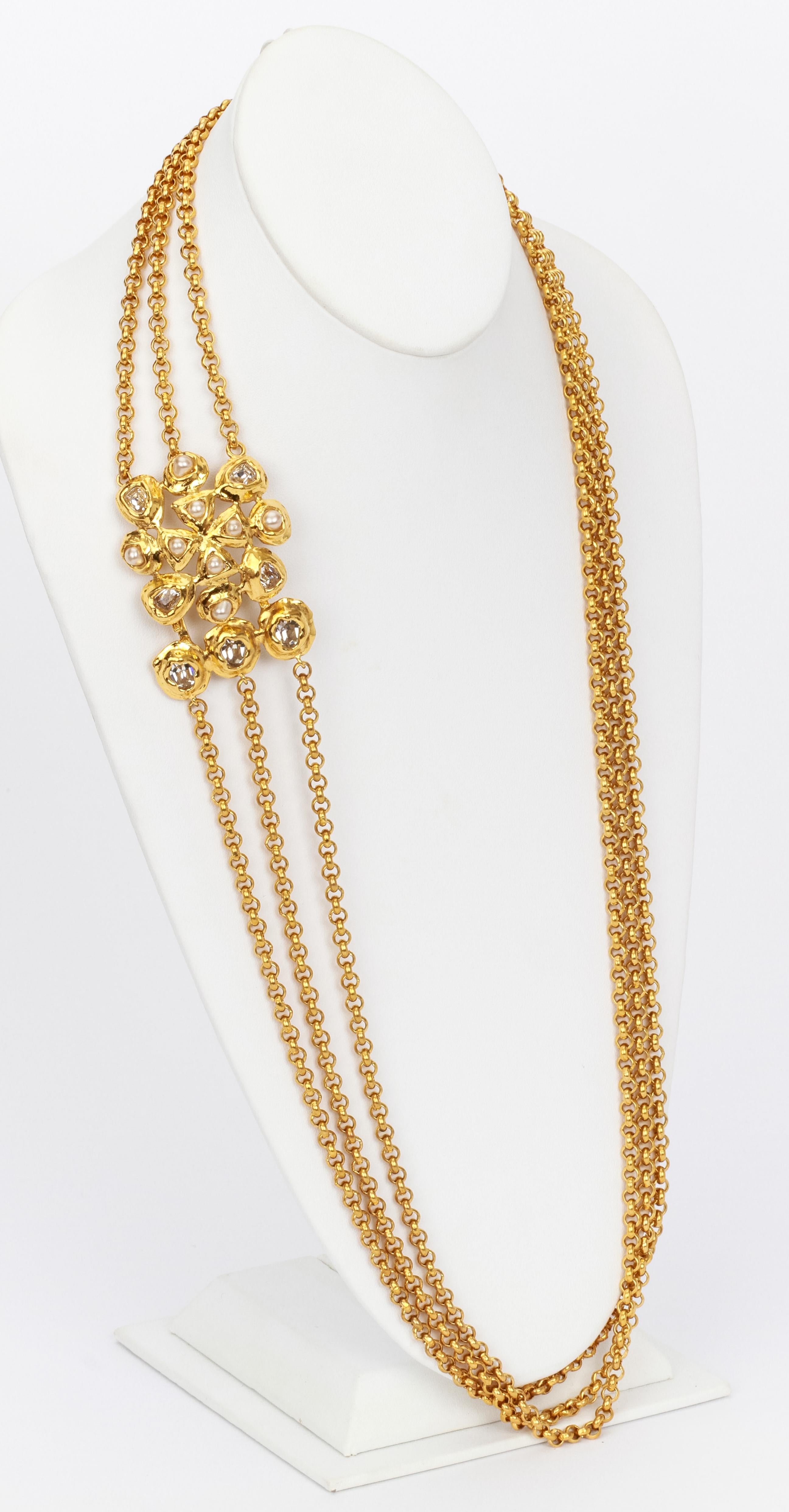 Chanel gold necklace with three chains and elaborate decorative clasp featuring cross with pearls surrounded by oval cut stones, all in abstract shape gold bezel settings. Comes with original pouch.