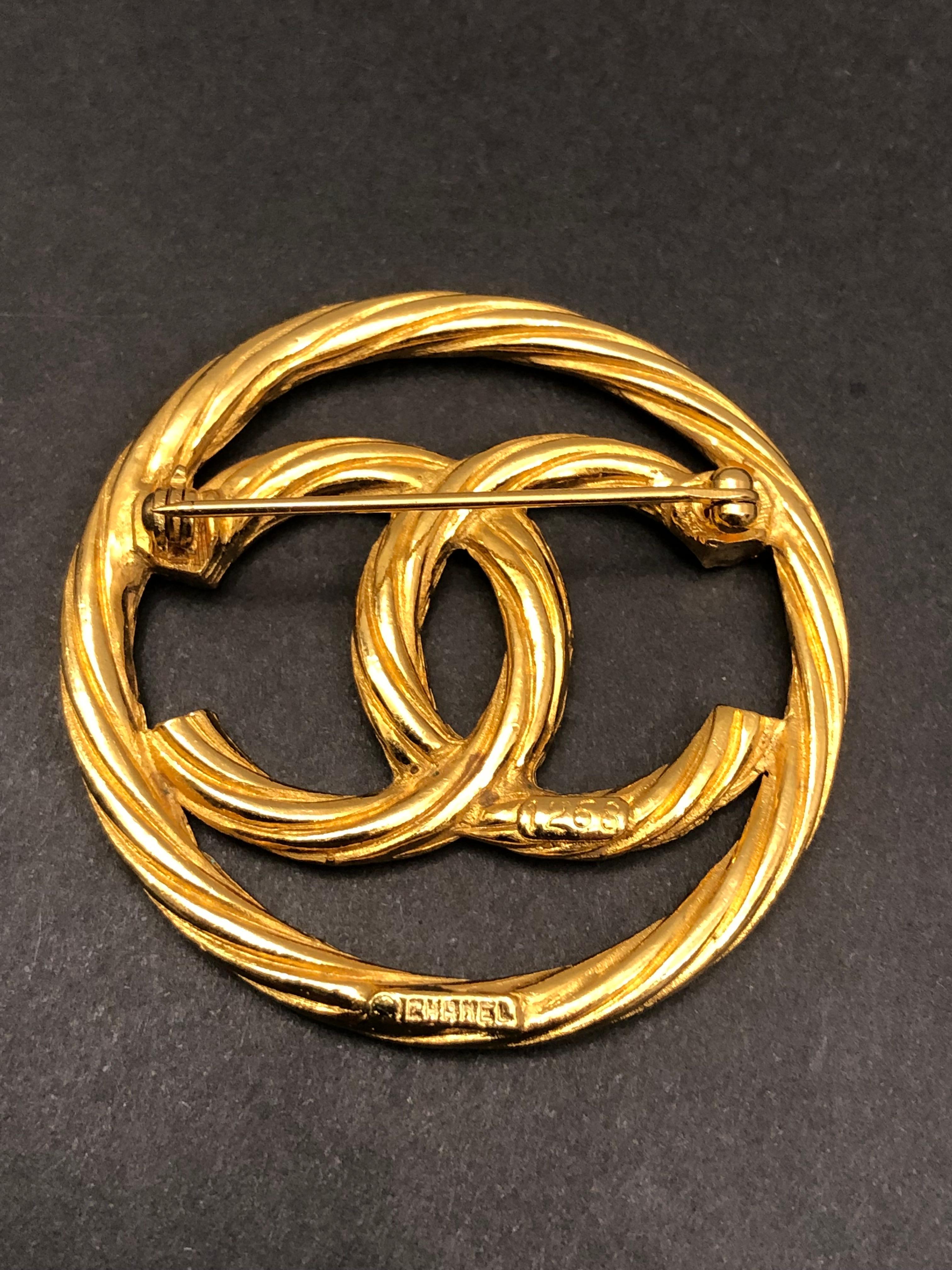 This vintage CHANEL gold toned brooch is crafted of gold plated metal in rope sling pattern featuring a CC logo. Stamped CHANEL 1268. Measures approximately 4.3 cm in diameter. Comes with box. 

Condition: Excellent vintage condition with minimal