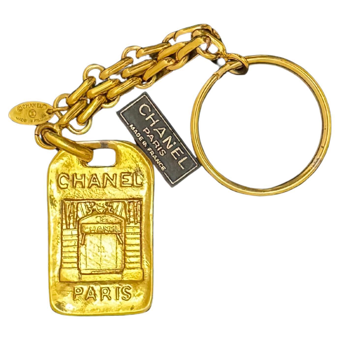 Este llavero vintage de CHANEL está fabricado en metal dorado con eslabones de cadena dorados, una anilla para llaves y un colgante de Chanel París en la puerta principal. Estampado CHANEL Made in France. La longitud mide aproximadamente 14 cm El