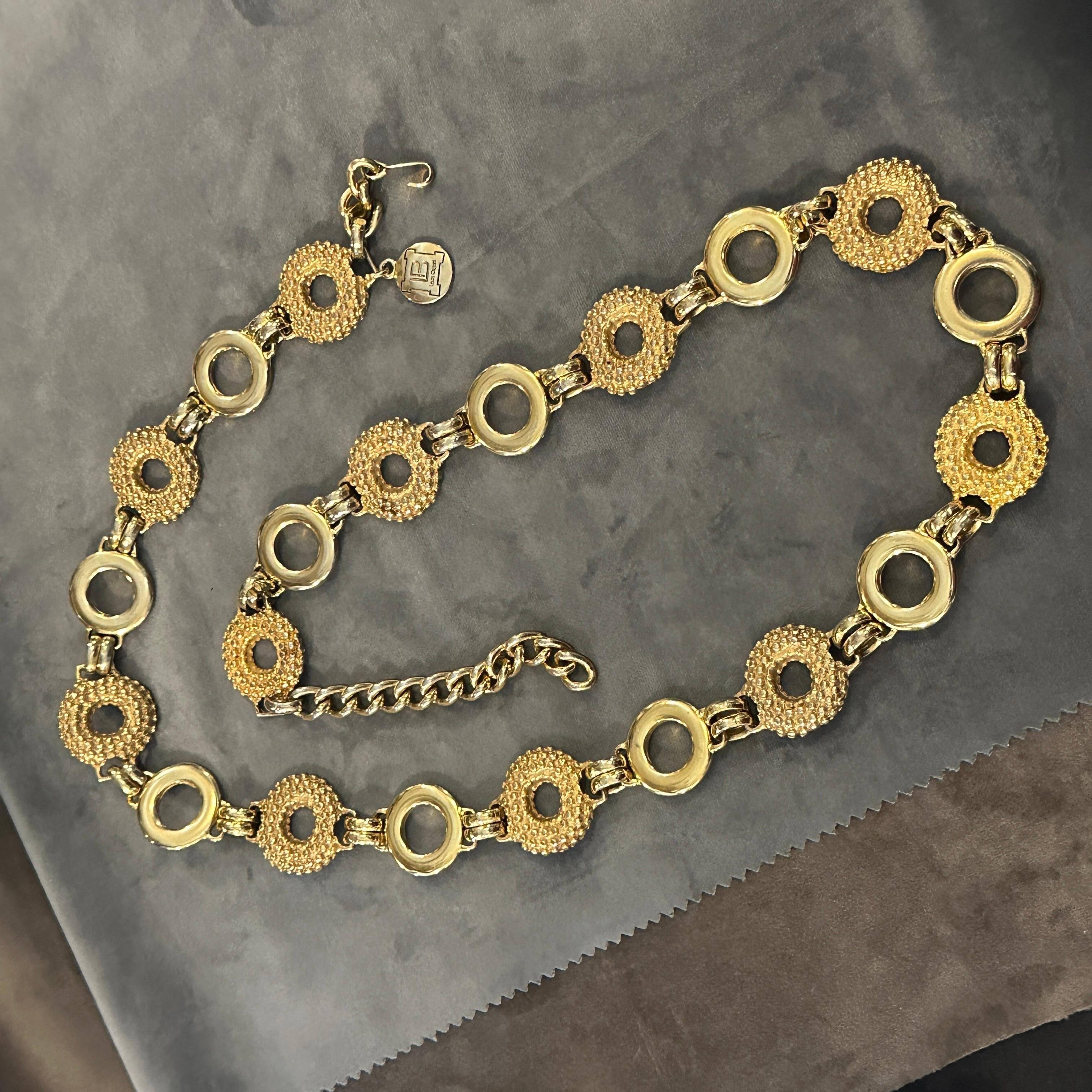 Il s'agit d'une ceinture vintage en métal doré des années 1980 de la créatrice italienne Laura Biagiotti. La ceinture présente un motif répétitif de maillons circulaires, alternant des disques texturés de couleur or et des maillons lisses à anneau