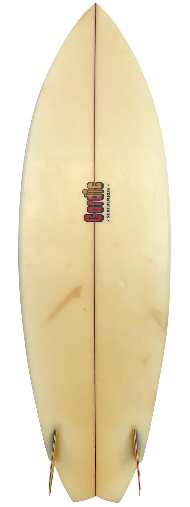 Mid-1980s Gordie Surfboards twin-fin fish short board. Features a winged swallow tail design, blue and orange airbrush, and original rainbow glass-on twin fin setup. A great example of a 1980s surfboard fish in all original condition.