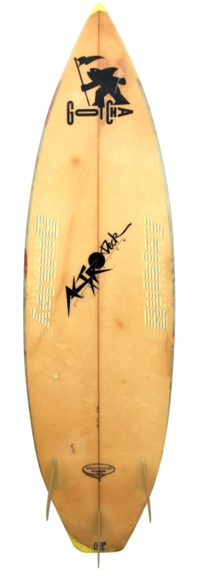1986 Gotcha Team thruster surfboard shaped by Brian Bulkley. Features an airbrush design indicative of the 1980s. Glassed-on thruster (tri-fin) setup with Gotcha Team and Astro Deck Team rider under-fiberglass lams. A great example of a sponsored