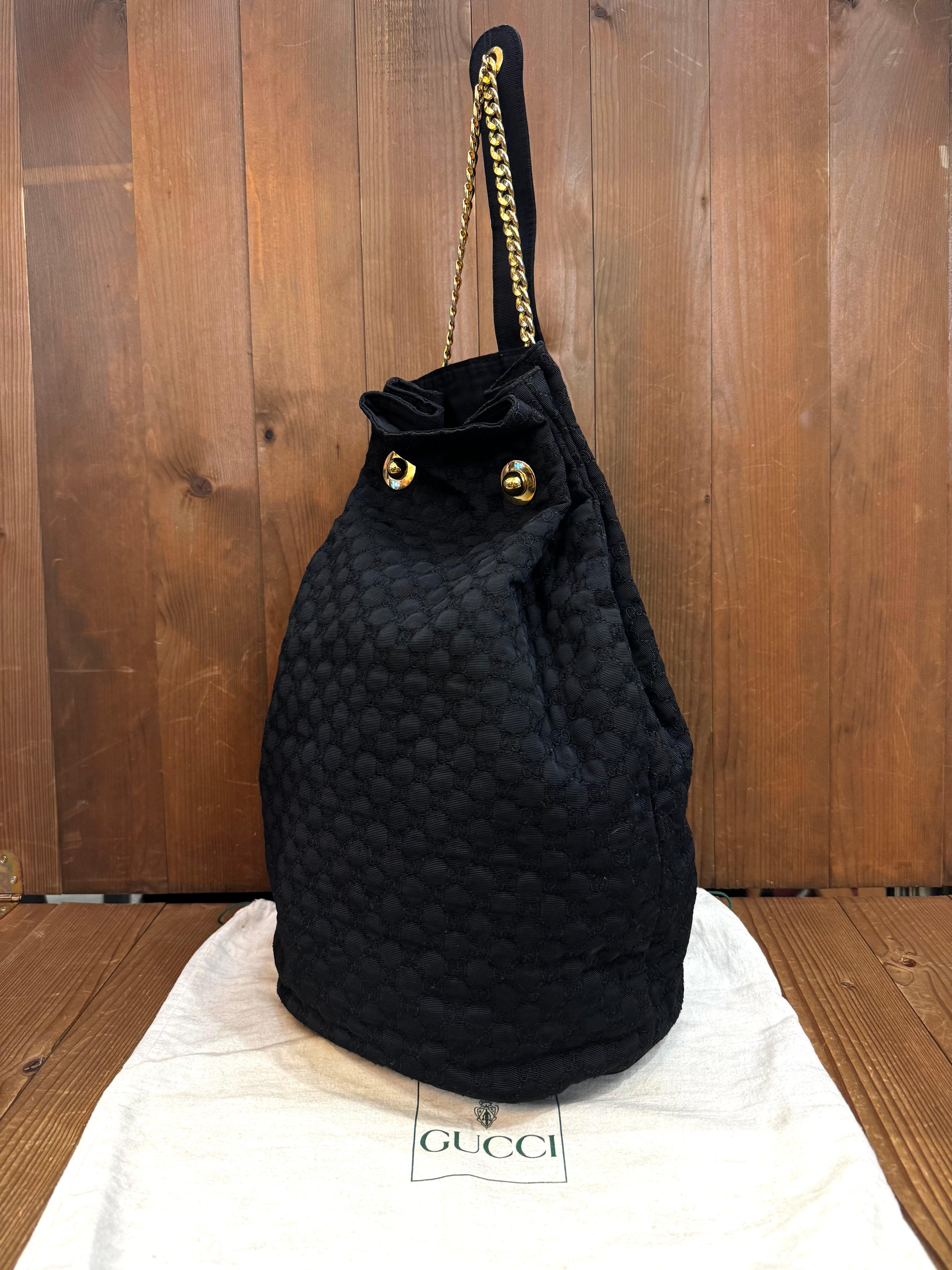 Ce sac à bandoulière seau GUCCI vintage est confectionné en tissu polyester noir brodé du monogramme GG et doté de chaînes d'épaule dorées. La fermeture par chaîne sur le dessus ouvre sur un intérieur en tissu noir doté d'une pochette zippée. Fait
