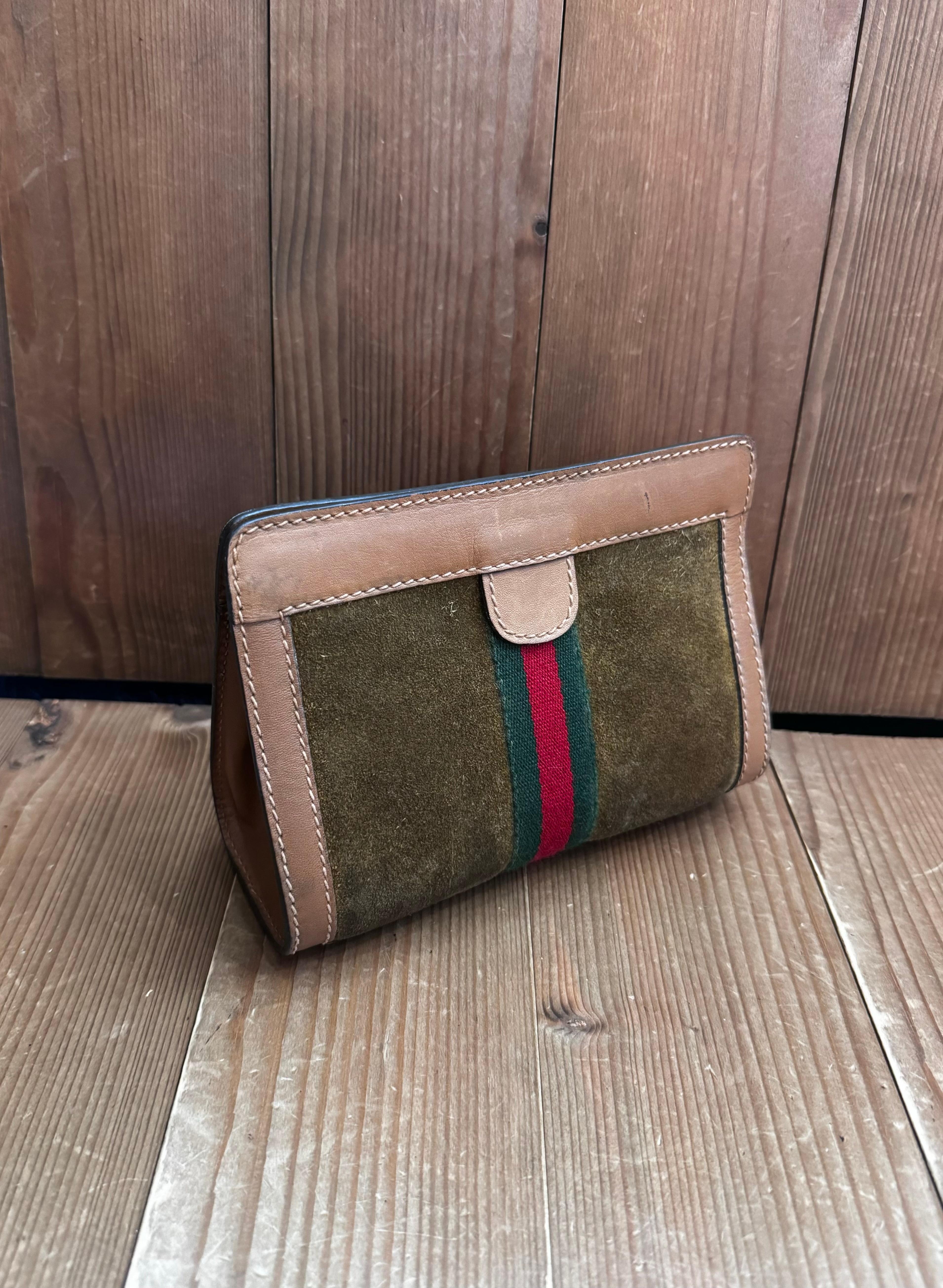 This vintage GUCCI pouch bag is crafted of suede and smooth calfskin leather in brown decorated with red/green stripe. Top velcro closure opens to laminated GG interior. Made in Italy. Measures approximately 7 x 5 x 3 inches.

Condition - Good