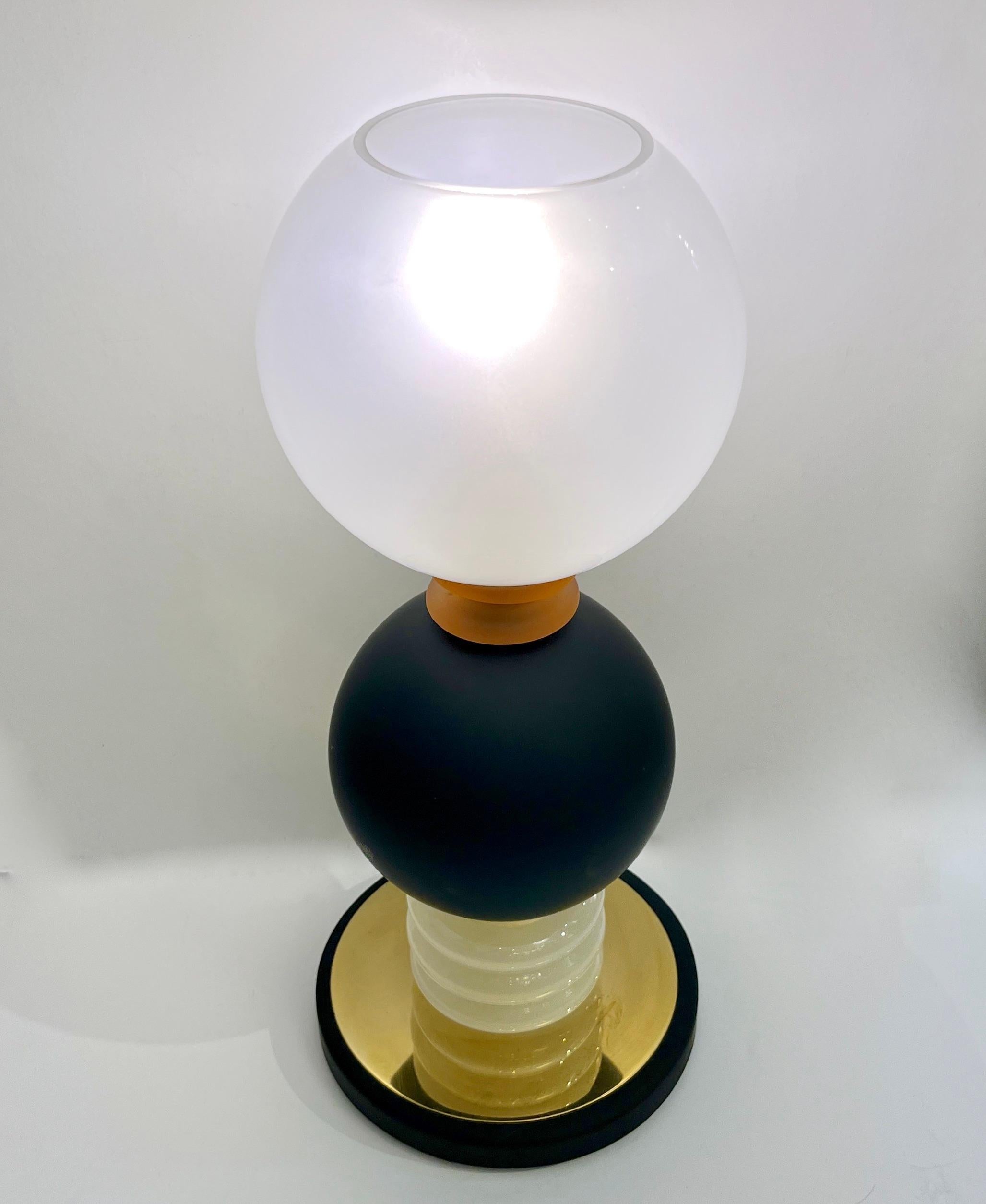 A unique pair of Made in Italy Tower Lamps, an attractive and functional design, with a round black cold-painted metal base covered with brass that supports a curved milky white Murano glass element, a matte black Murano glass sphere highlighted by