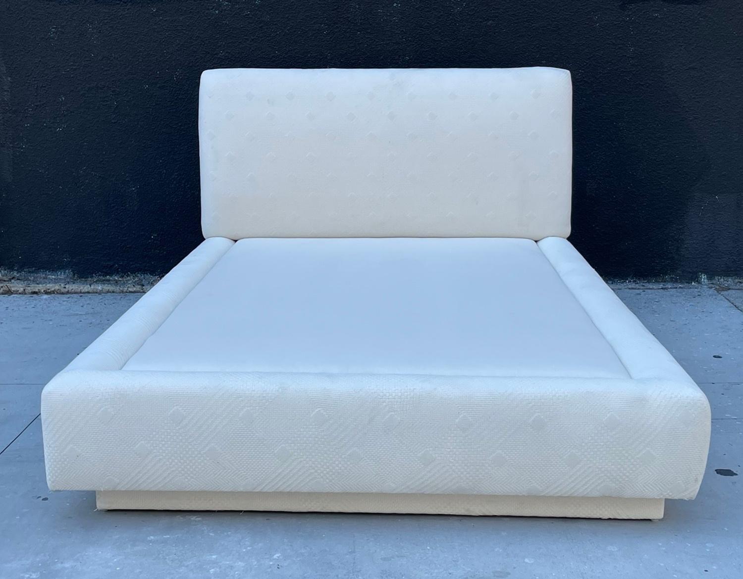 Un remarquable lit queen vintage fabriqué aux États-Unis dans les années 1980, doté d'une plate-forme à profil bas et d'une tête de lit intégrée. Ce cadre de lit sculptural est entièrement tapissé d'un tissu ivoire texturé avec un motif géométrique