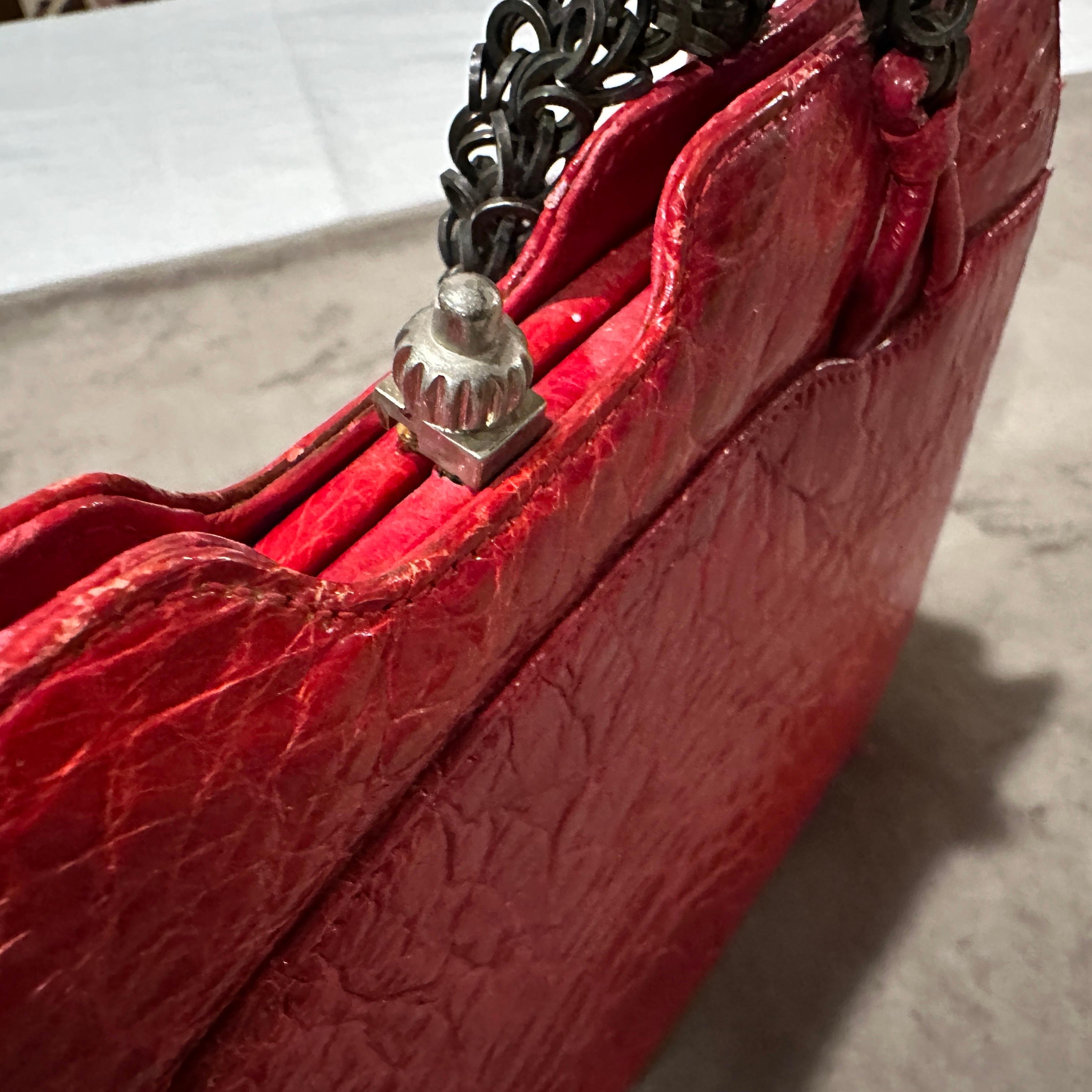 This stunning 1980s vintage Italian evening bag is a bold and elegant statement piece. The body of the bag is crafted from luxurious, glossy red leather embossed with a crocodile-style texture, giving it an exotic and high-end appeal. A vibrant,