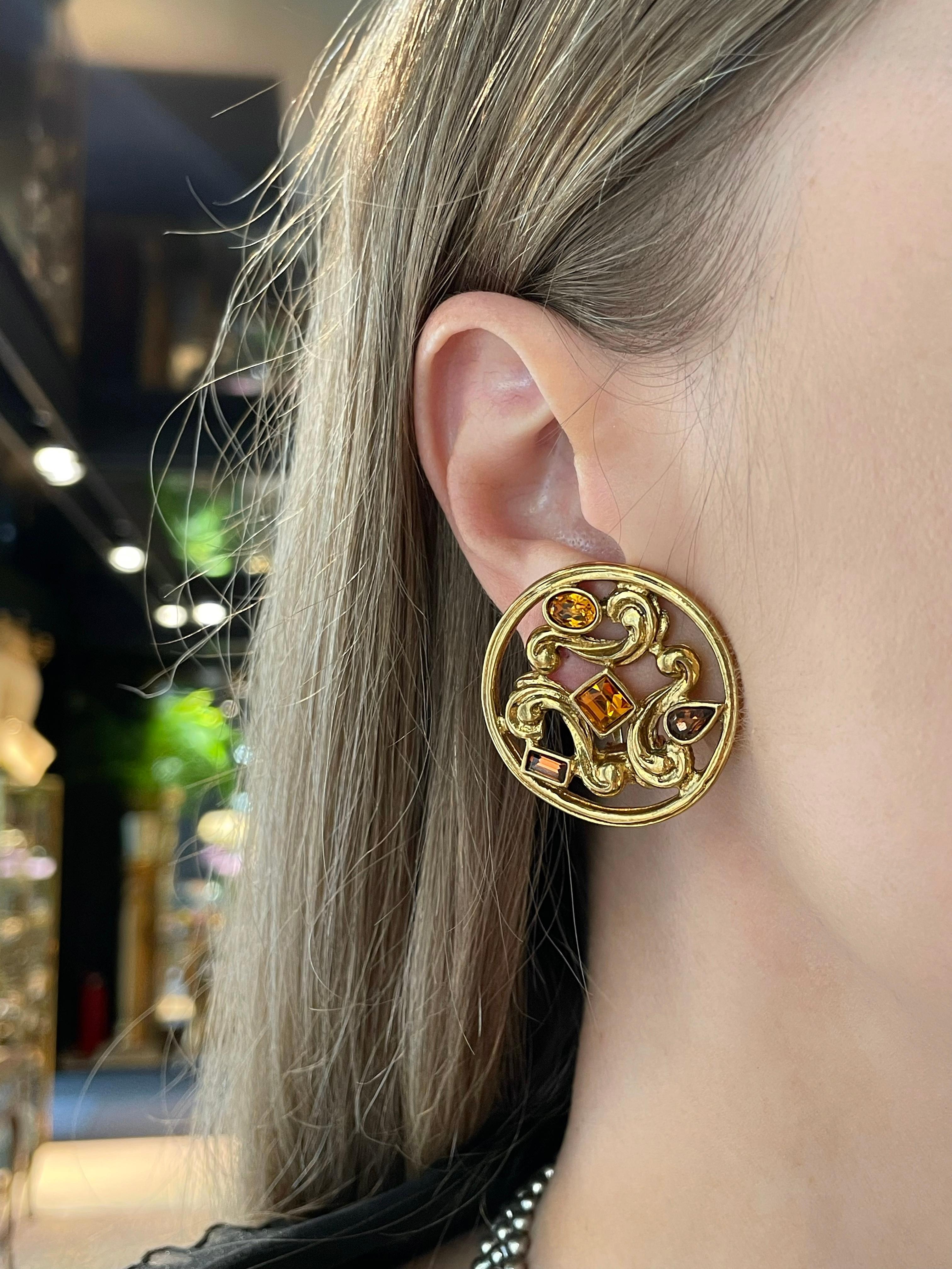 Dies ist ein Paar goldfarbene, runde Ohrringe im Barock-Design mit Clip. Das Stück ist vergoldet, entworfen von YSL in den 1980er Jahren.

Er ist mit orangefarbenen und braunen Kristallen besetzt.

Unterzeichnet: 