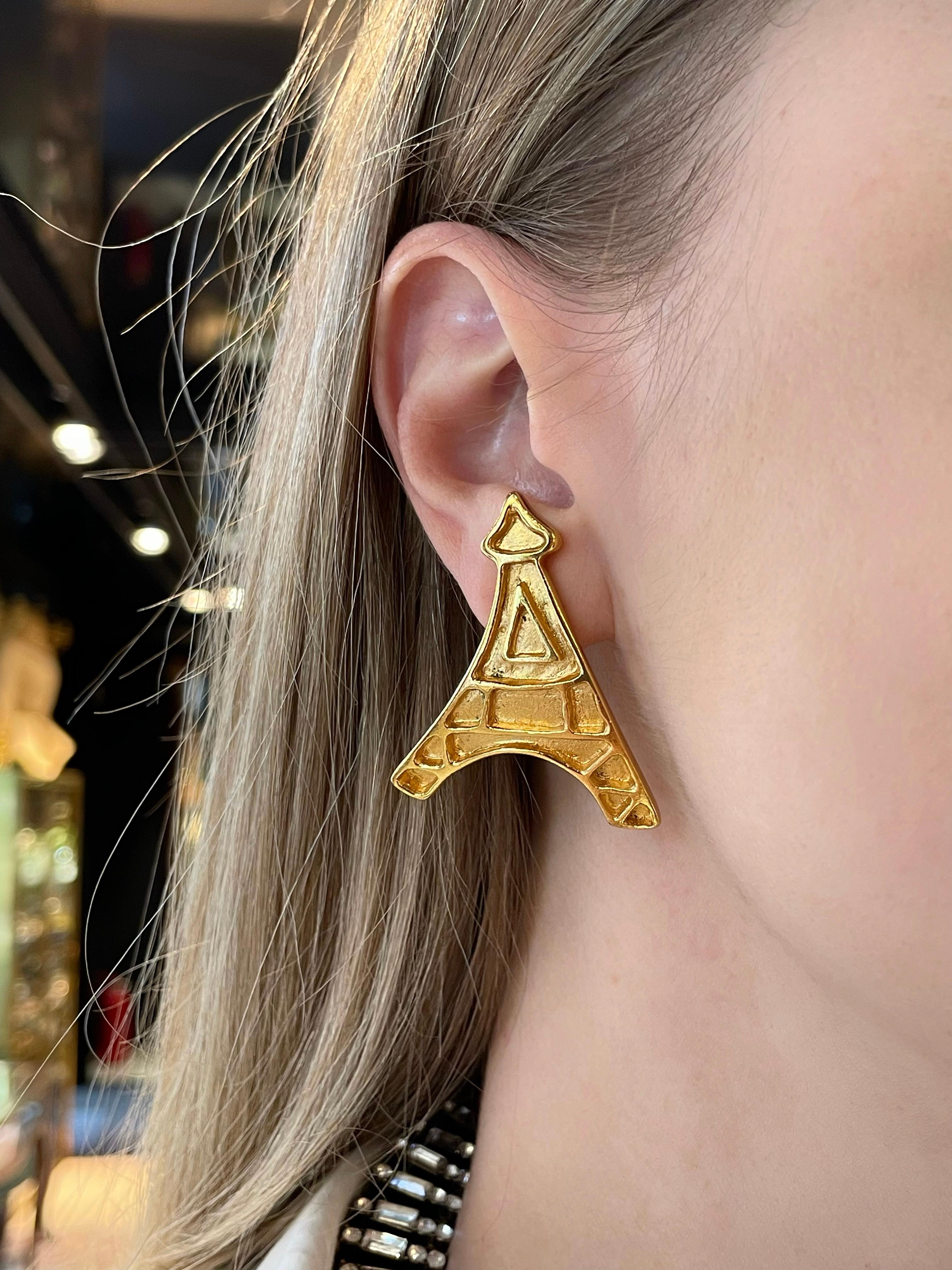 Il s'agit d'une paire de boucles d'oreilles à clip vintage en ton or représentant la silhouette de la tour Eiffel. La pièce est plaquée or, conçue par YSL dans les années 1980.

Marques : 