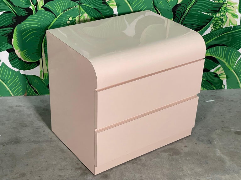 80s Era nightstand features smooth waterfall front and a solid plinth style base. Styling reminiscent of Karl Springer. Good condition with only minor imperfections and drawers operate like new. As with all our vintage items, may exhibit scuffs,
