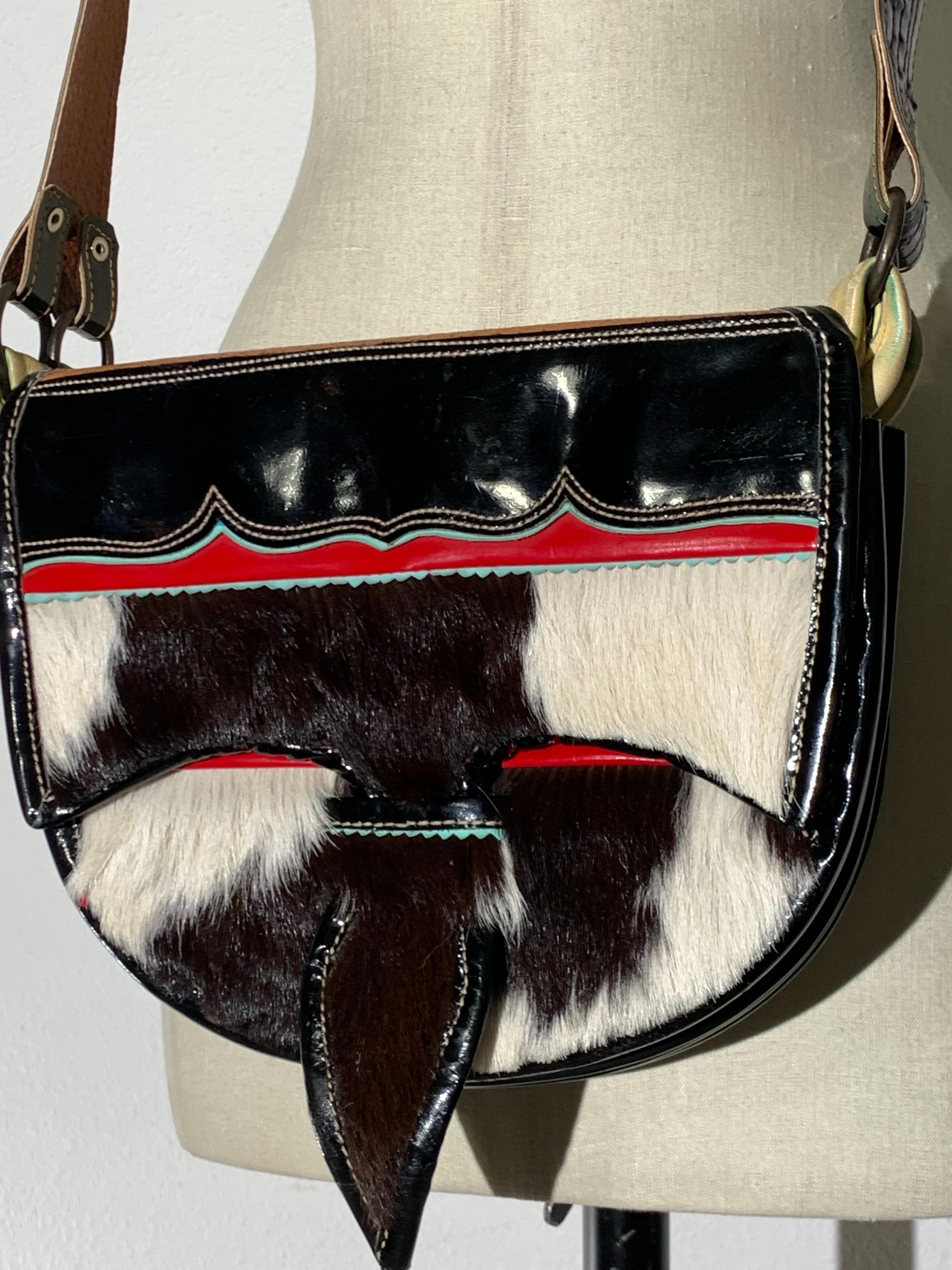 1980s Western-Inspired Black/White Cowhide & Patent Leather Saddle Shoulder Bag: Accordion-style expanding compartments with sliding tab closure on flap. Wide adjustable shoulder strap. Red leather interior lining. Zippered inside pocket. Medium