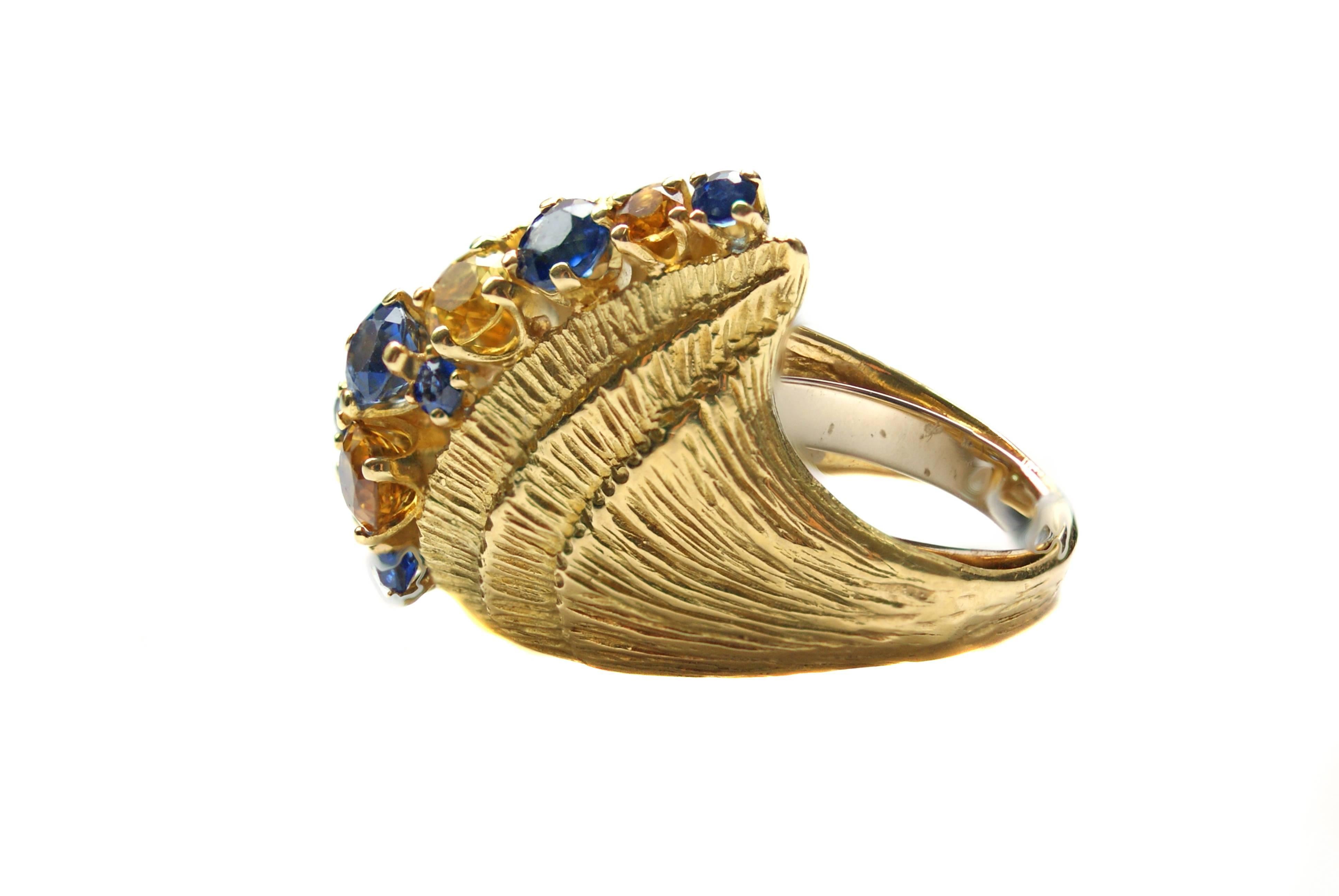 Fashionable and bold 1980s ring centrally set with 4 yellow and golden color round cut sapphires and 8 intense blue color round cut sapphires. The incredibly well hand-crafted 18 karat yellow gold ring features 4 steps of finely hand engraved