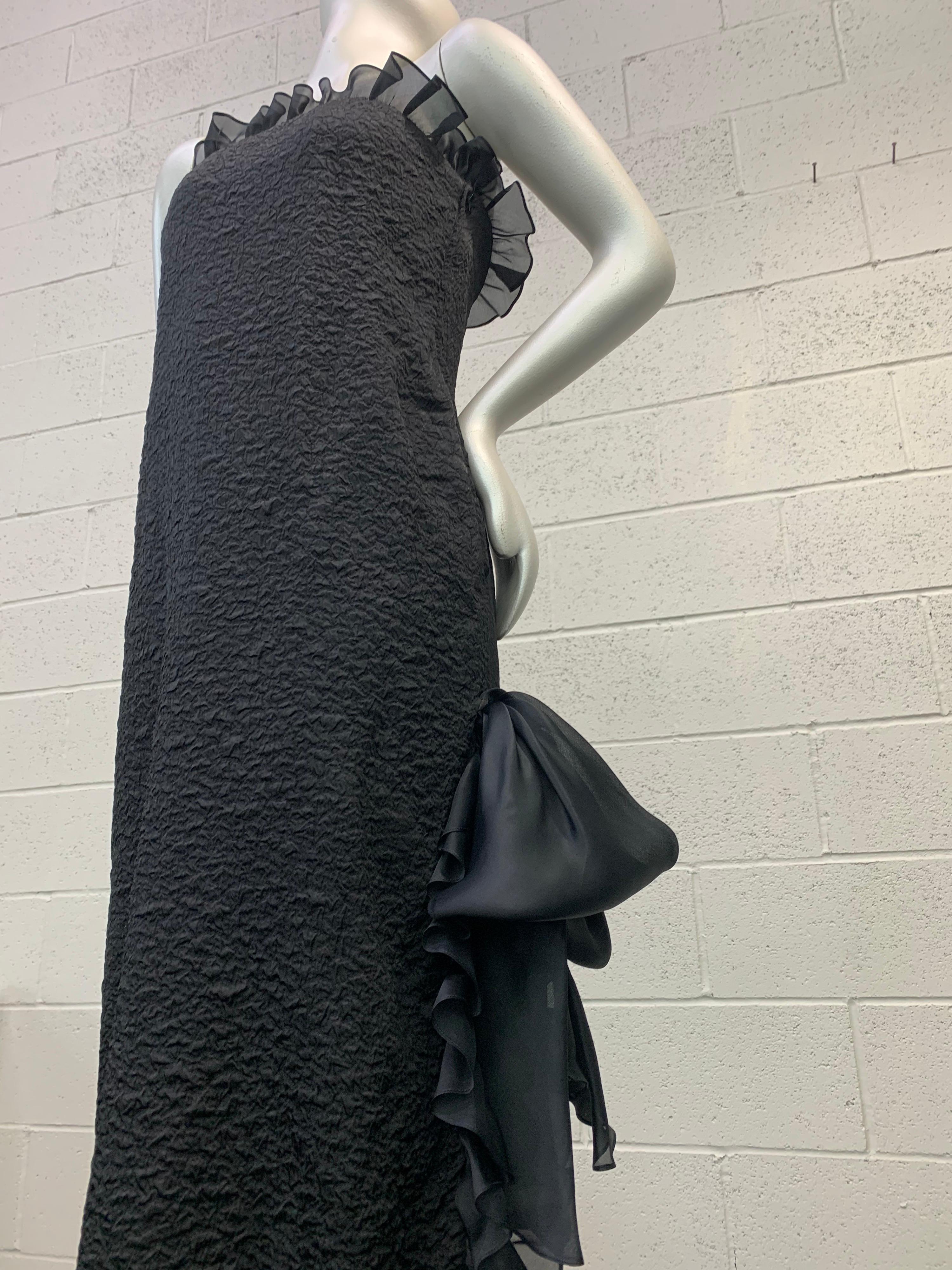 An elegant 1980s Yves Saint Laurent black rayon and acetate textured crepe gown: Simple in silhouette, this slim gown brings focus to the face with an organza ruffle running completely around décolletage and down one side along high side slit.