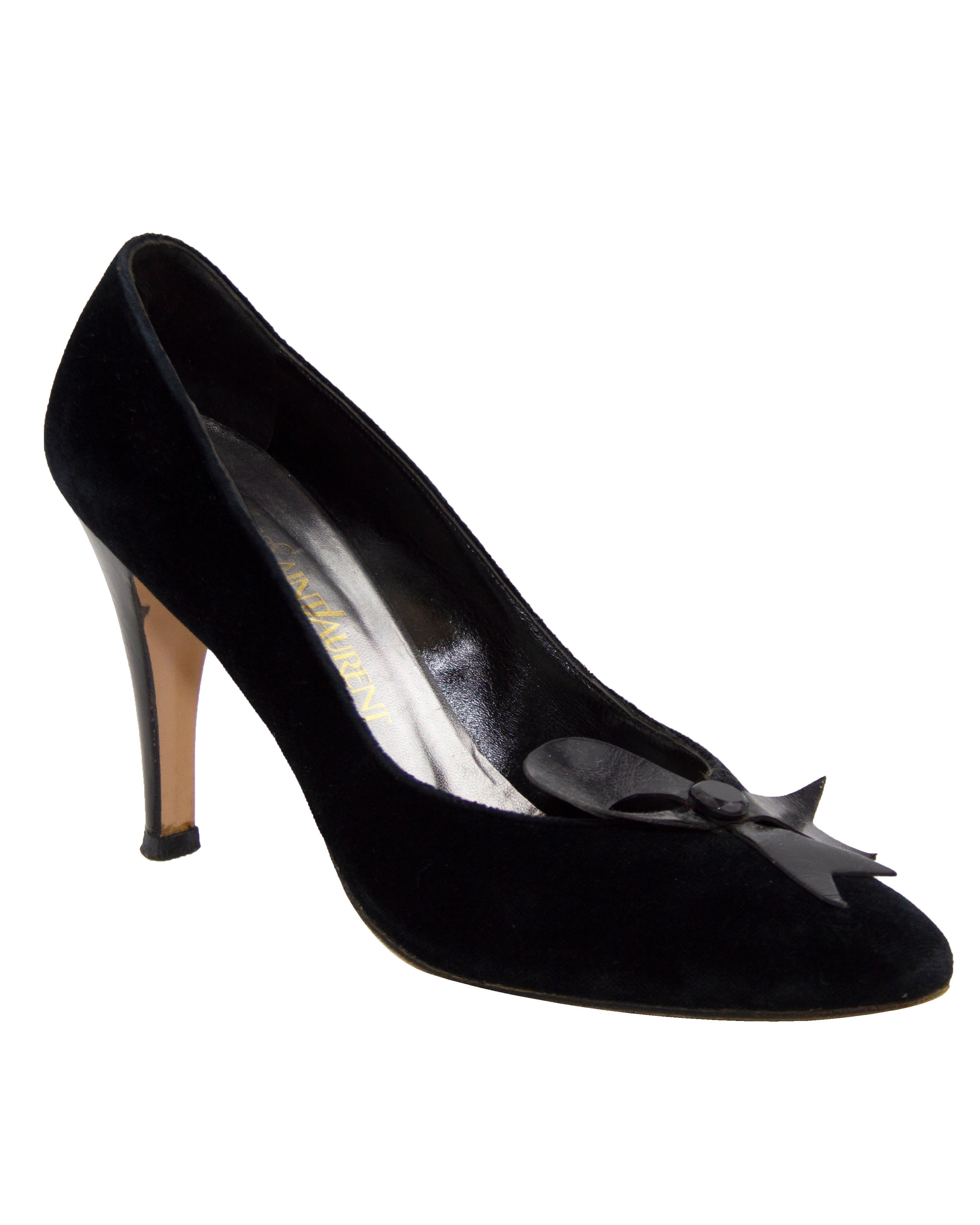 Very early pair of Yves Saint Lauren pumps. Circa the 1980s, these heels have a cut black velvet body with a black patent leather half bow detail on the toe box and black leather heels. The bows are embellished with a single black faux jewel in the