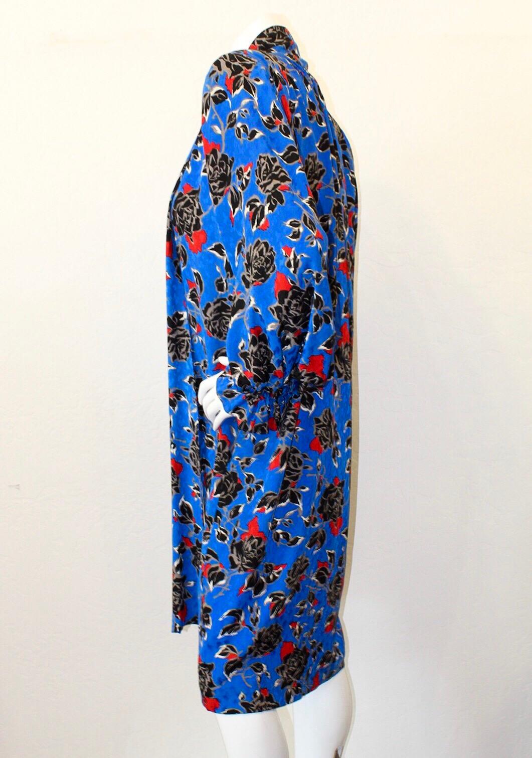 Show off your inner chic 80's girl with this amazing YSL dress! Features a black and red floral pattern on top of the contrasting overall bright royal blue color. Includes bishop sleeves with a ruffle cuff and a pussycat bow neck tie. The perfect