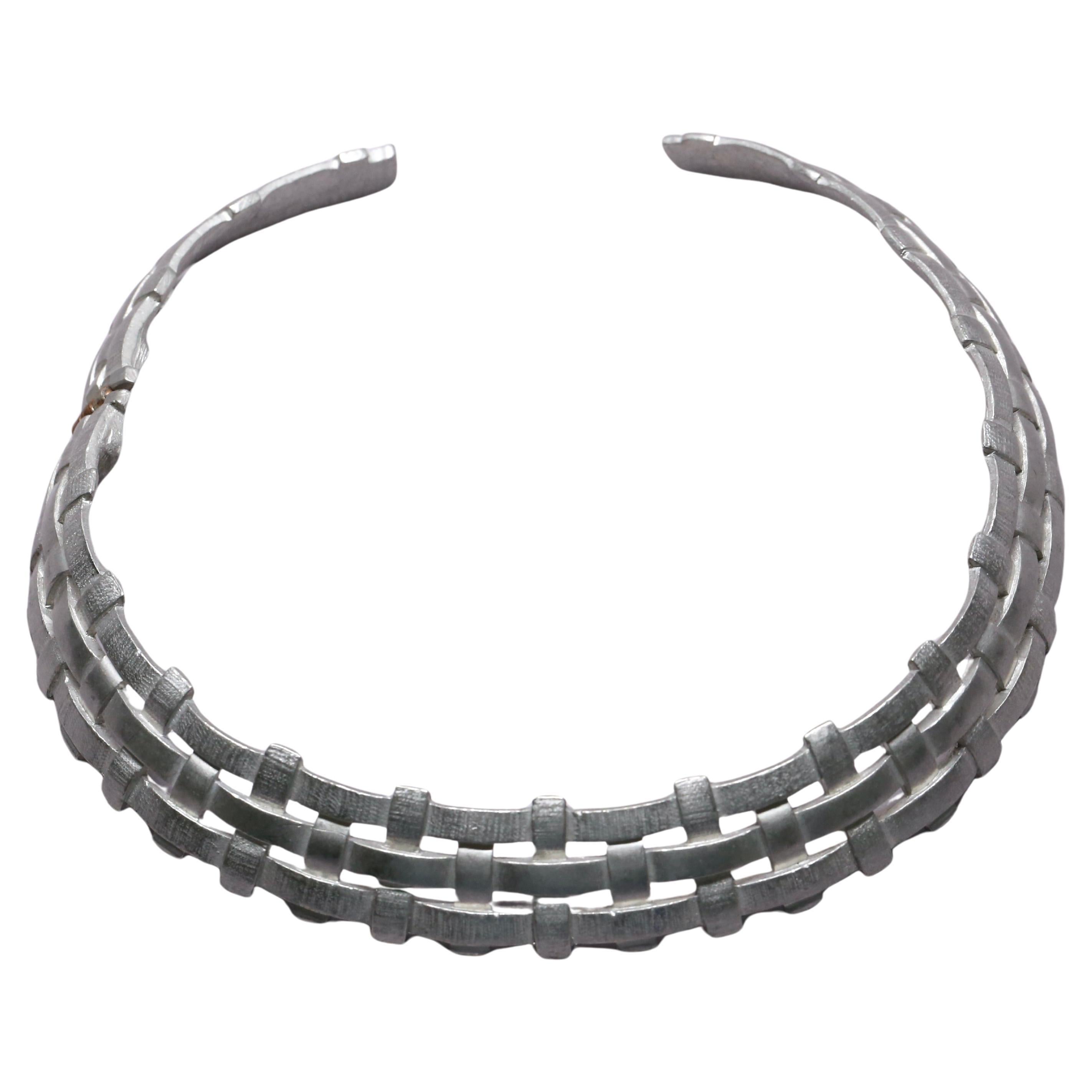 This vintage Saint Laurent necklace features a sculptural, woven metal design in a silvery, matte finish. The piece is structured as a rigid collar or choker, composed of interlaced rectangular links that create a basket-weave texture. The geometric