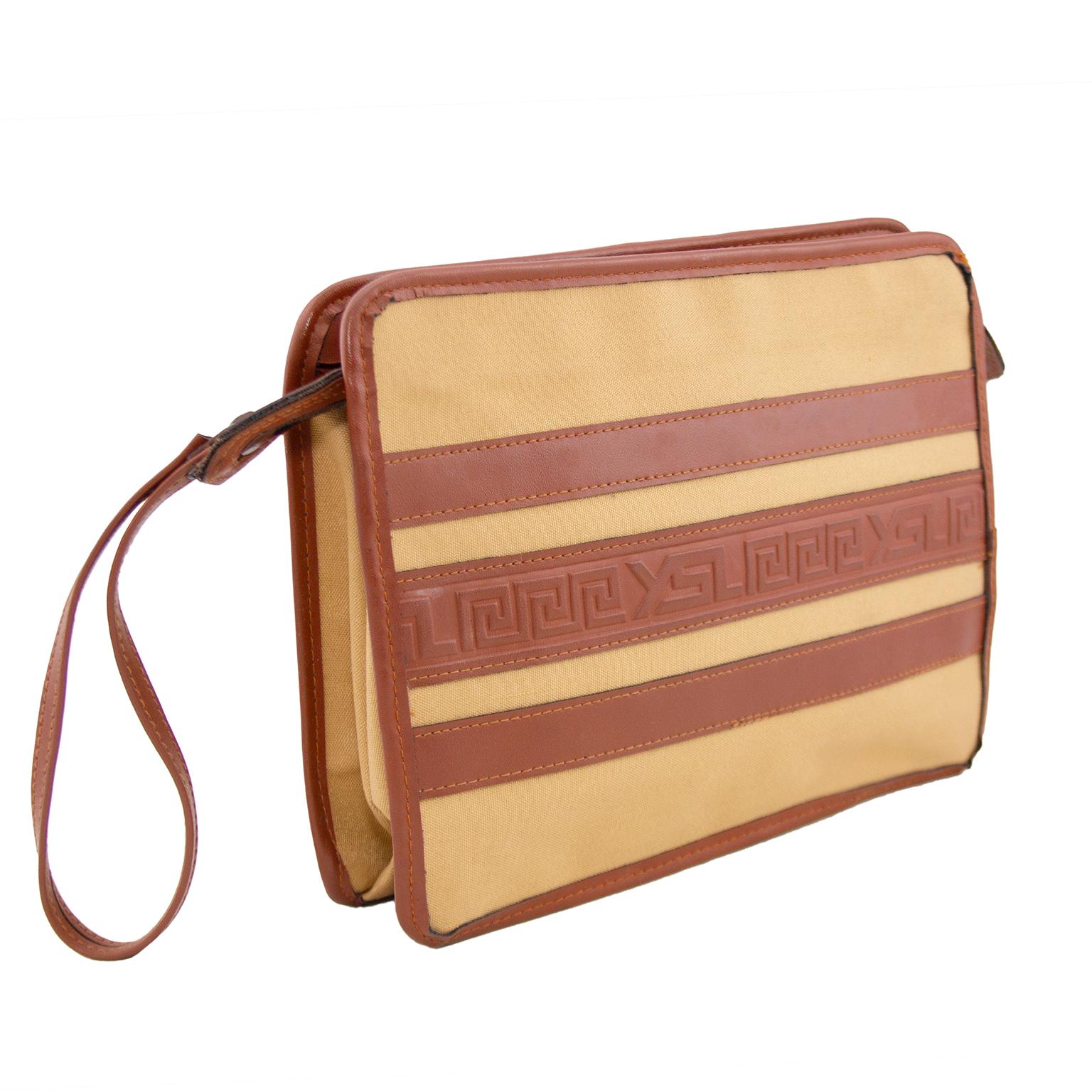 1980s Yves Saint Lauren tan leather and beige canvas clutch/wristlet. Rectangular shape with tan leather trim and horizontal stripes of tan leather. Middle stripe is embossed with greek key details with YSL throughout. Brown top zipper closure and