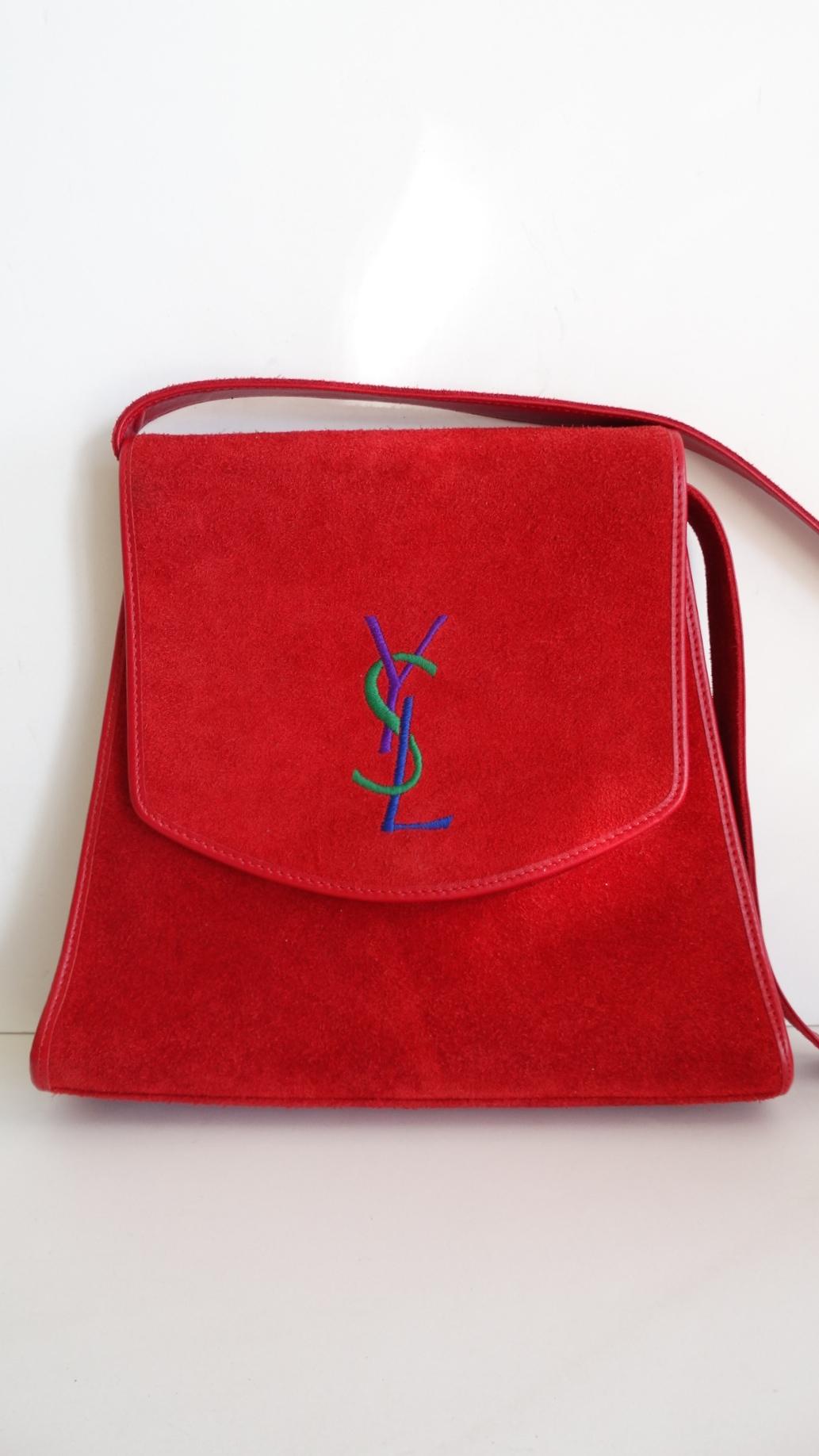 The Most Adorable Bag Is Here And We Are Obsessed! Circa 1980s, this Yves Saint Laurent cross body bag is lipstick red suede and includes a tonal leather trim. Features a contrasting purple,green and blue YSL stitched on the front. Includes gold