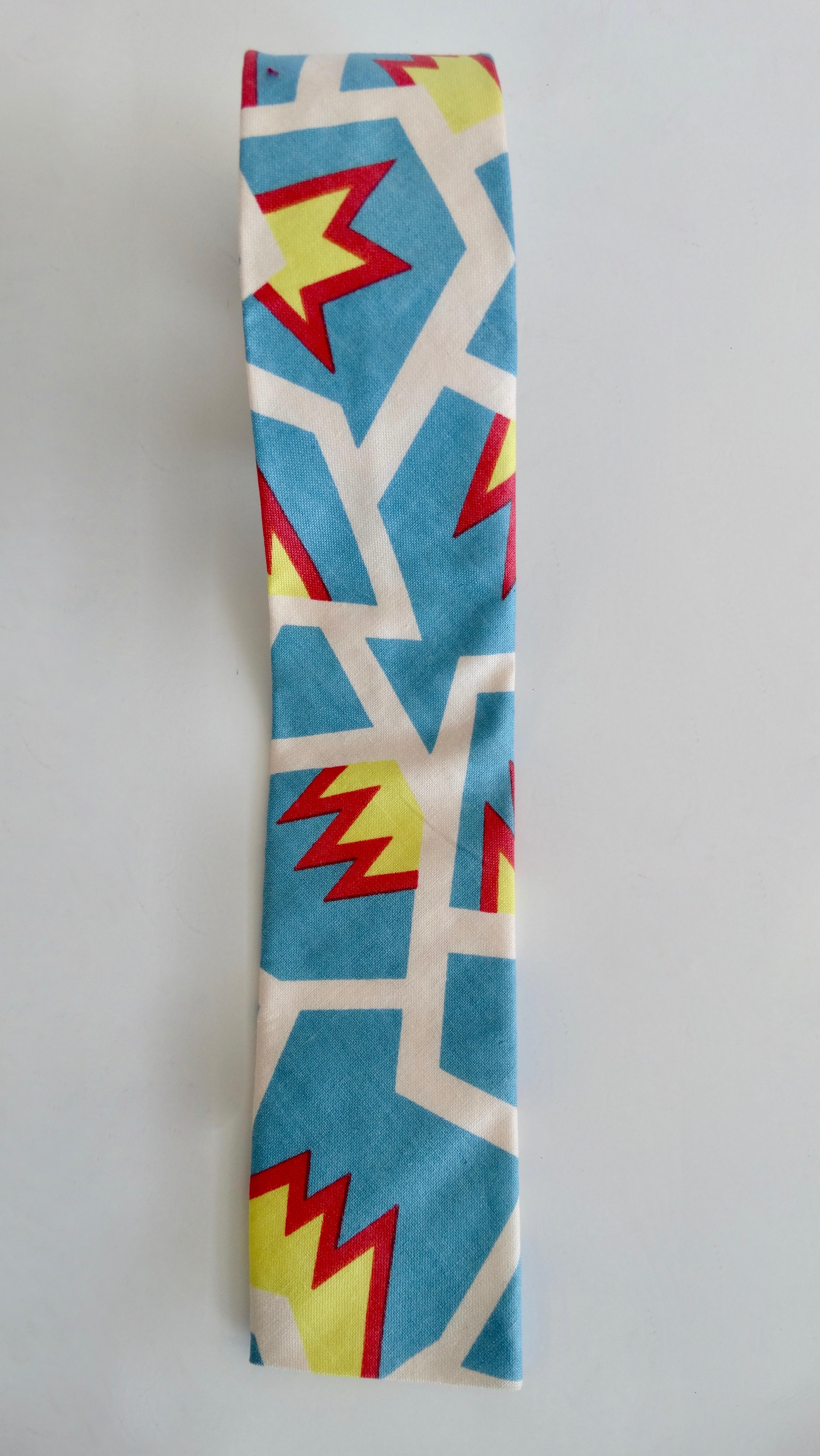 Elevate your look with this amazing Memphis Milano tie! Circa 1981, this skinny square Cotton tie features an abstract design created by Memphis Milano founding member, Nathalie Du Pasquier. Comprised of multi-directional white lines with red/yellow