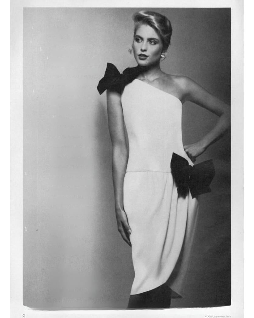 1983 Oscar de la Renta 'Miss D' white asymmetrical above-knee dress with black silk-satin bows at strap and hip. Drop waist one-shoulder dress with silk crepe fabric that drapes throughout hips. Concealed back zip closure. As sen in B. Altman & Co