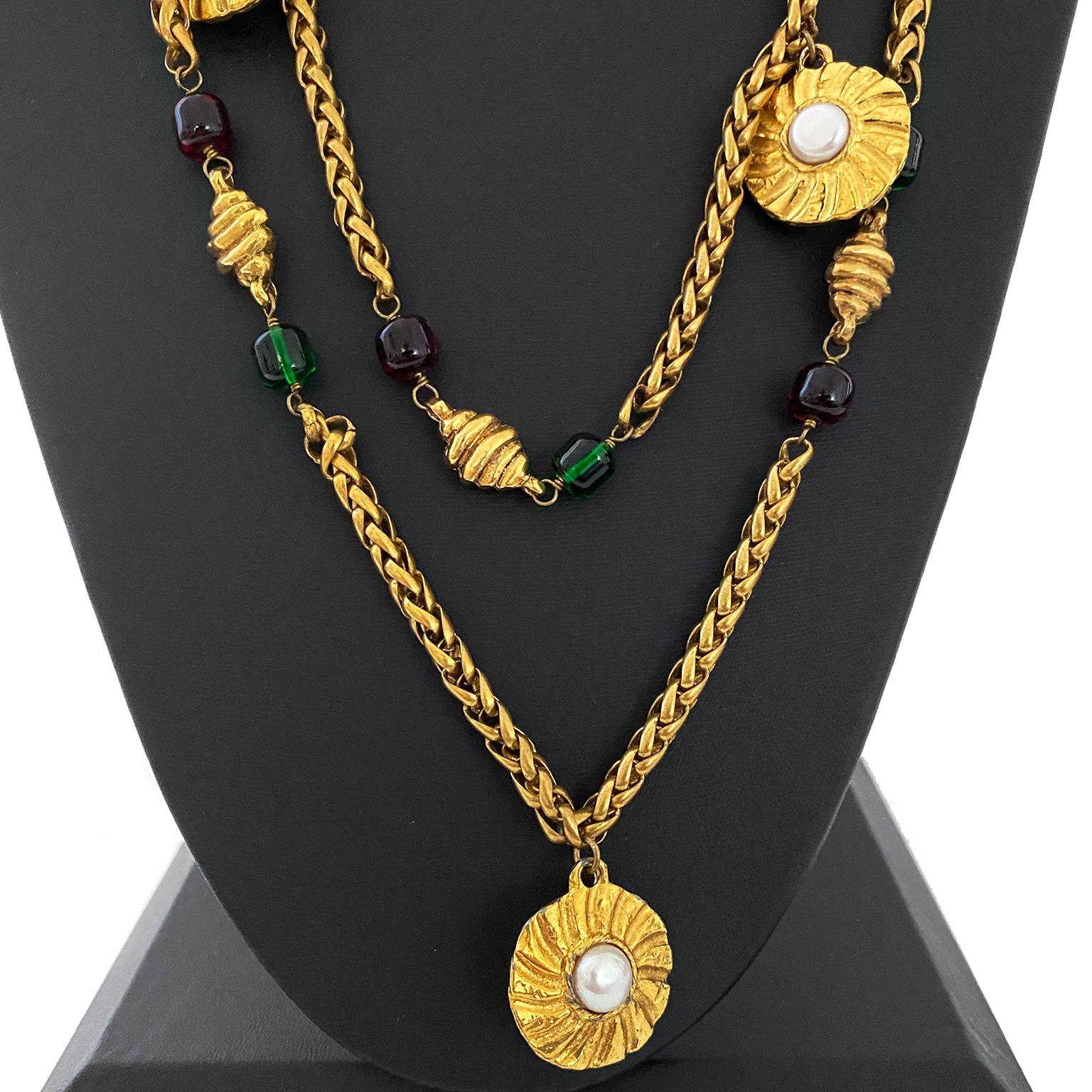 Spettacolare, lussuosa e pesante collana Chanel del 1984. Catena a palma in tonalità oro impreziosita da grandi dischi rotondi articolati in metallo dorato e centri di perle finte, piccoli ciondoli dorati a forma di cornetto collegati a perline