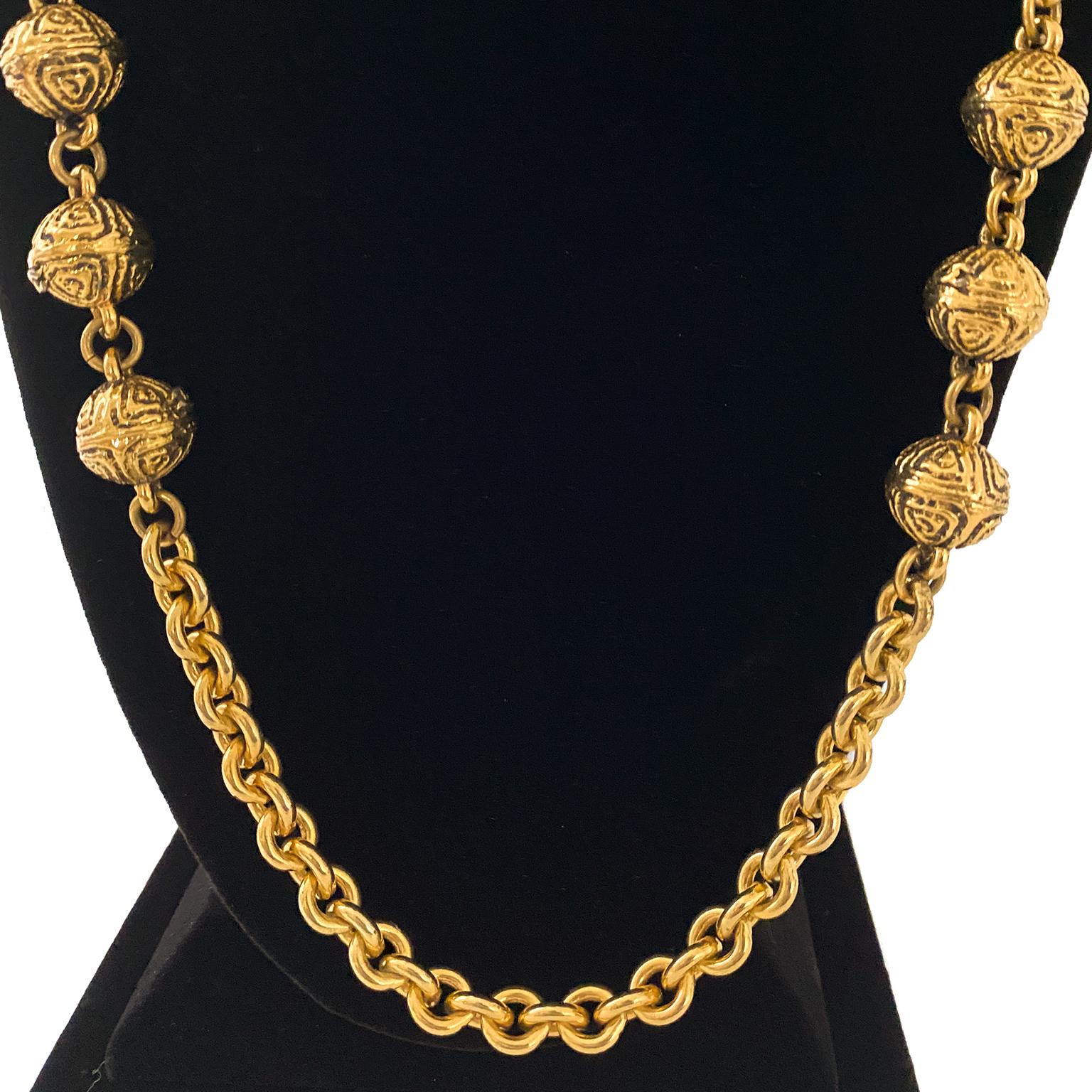 Chanel gold tone thick chain link necklace from 1985. Six intricately detailed gilded beads on either side. Hook and eye clasp. Hanging oval stamped Chanel brand tag. Can be worn long or wrapped to make it a multi-layer chain. Excellent vintage
