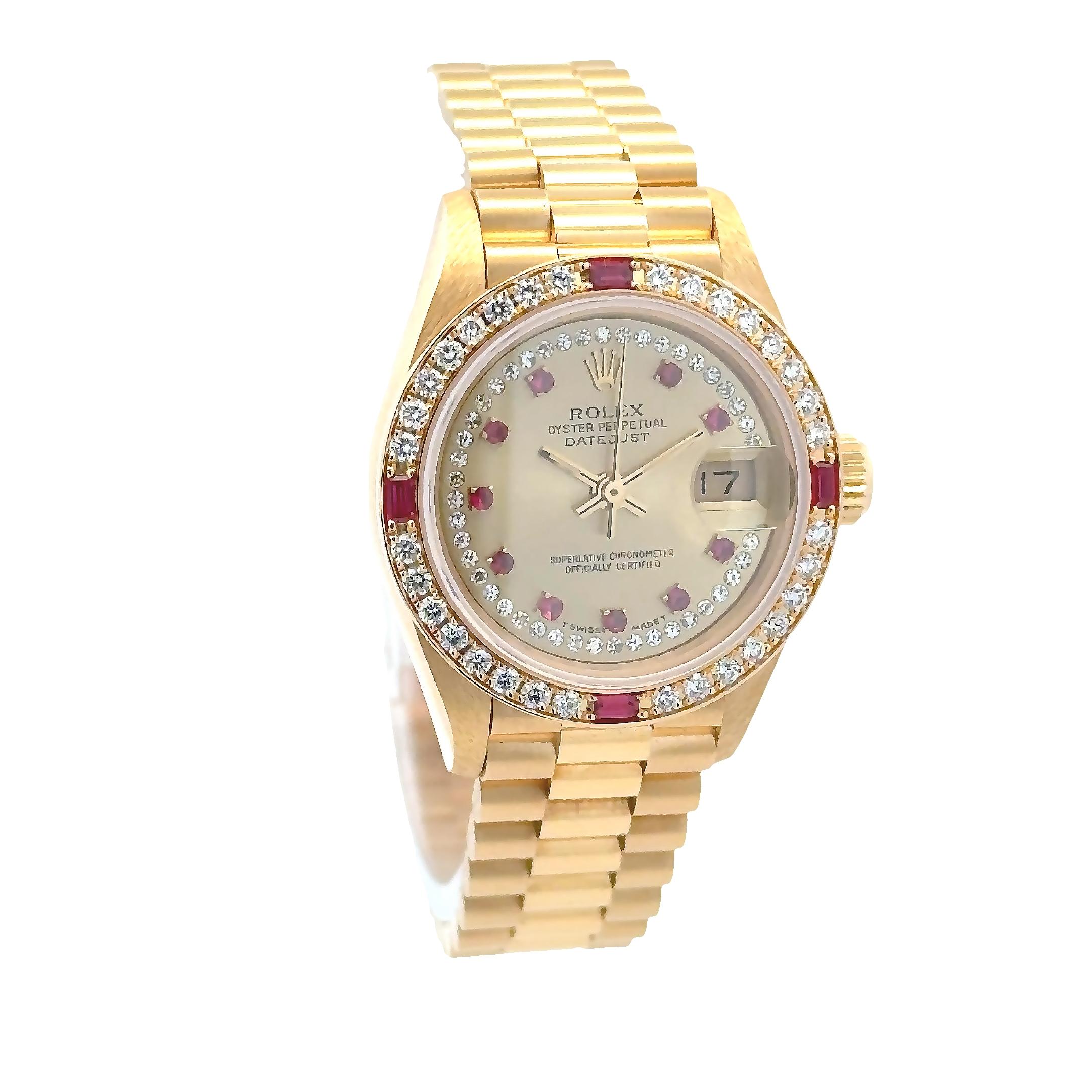 Cette Rolex Datejust de 1985 est une luxueuse pièce d'horlogerie pour dames, fabriquée en or jaune 18 carats, avec un boîtier de 26 mm, un cadran champagne classique et un bracelet président. Ornée de diamants et de rubis sertis en usine, elle est